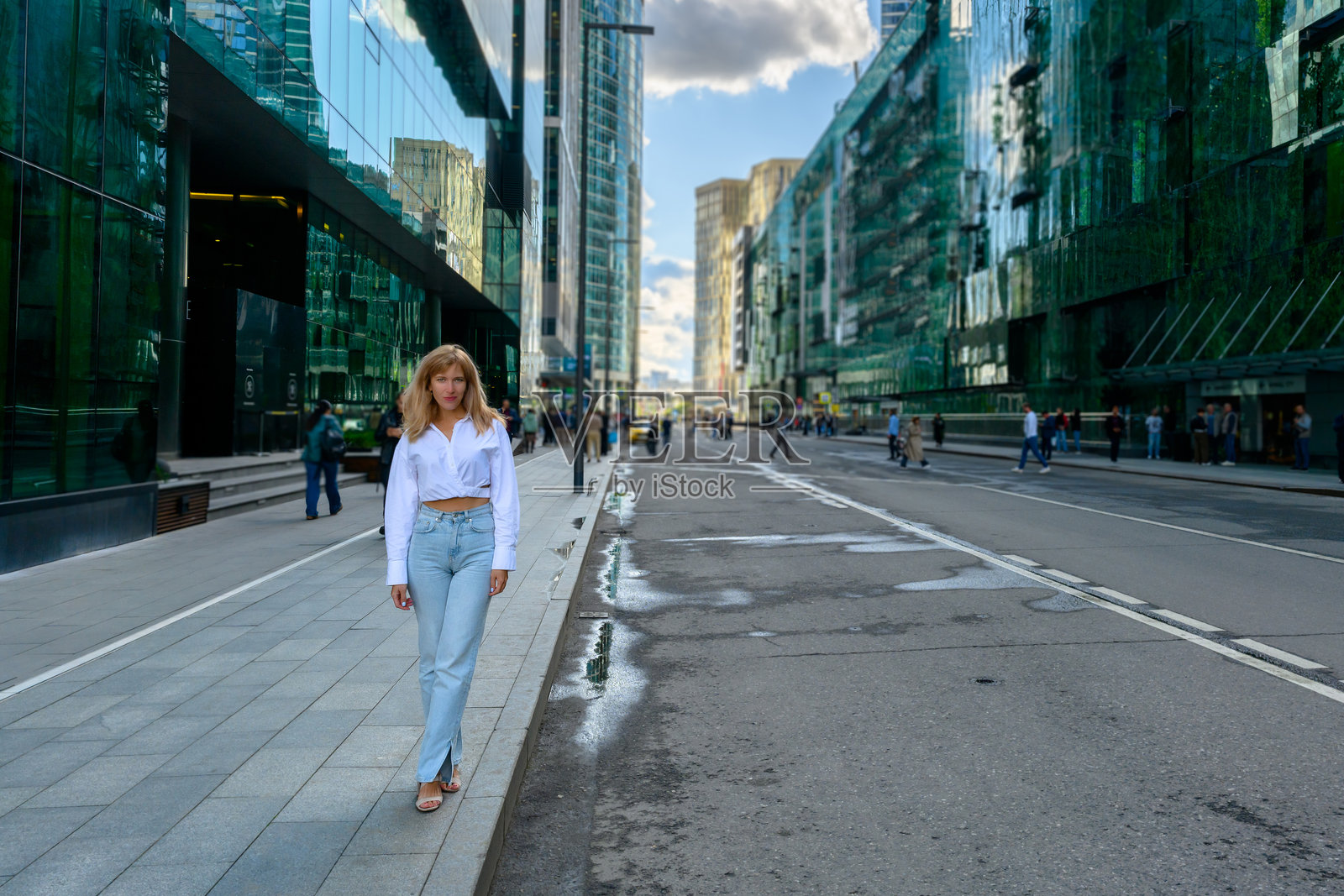 午后阳光下,在充满活力的城市街道上,人们漫步于高耸的玻璃建筑旁。照片摄影图片