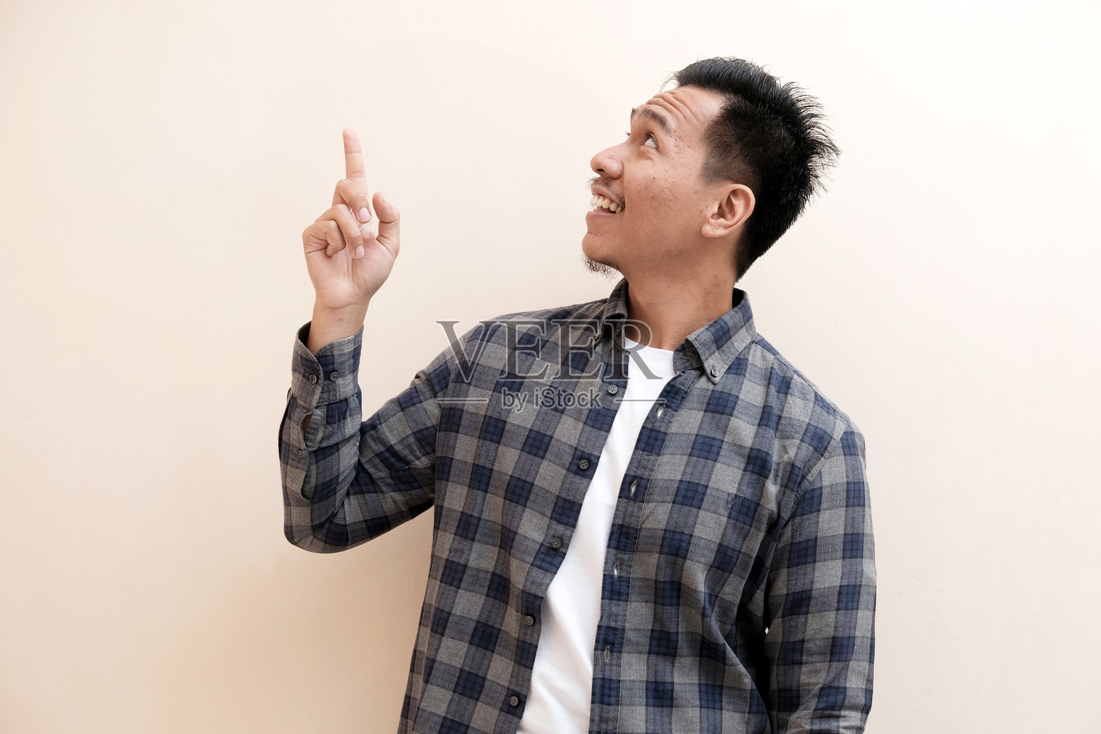 东南亚男子穿着法兰绒衬衫,表情愉悦,兴奋地向右边指着。照片摄影图片
