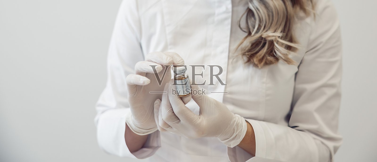 一位女性美容师在临床环境中手持一剂疫苗,她穿着手套和白大褂,准备进行注射。照片摄影图片
