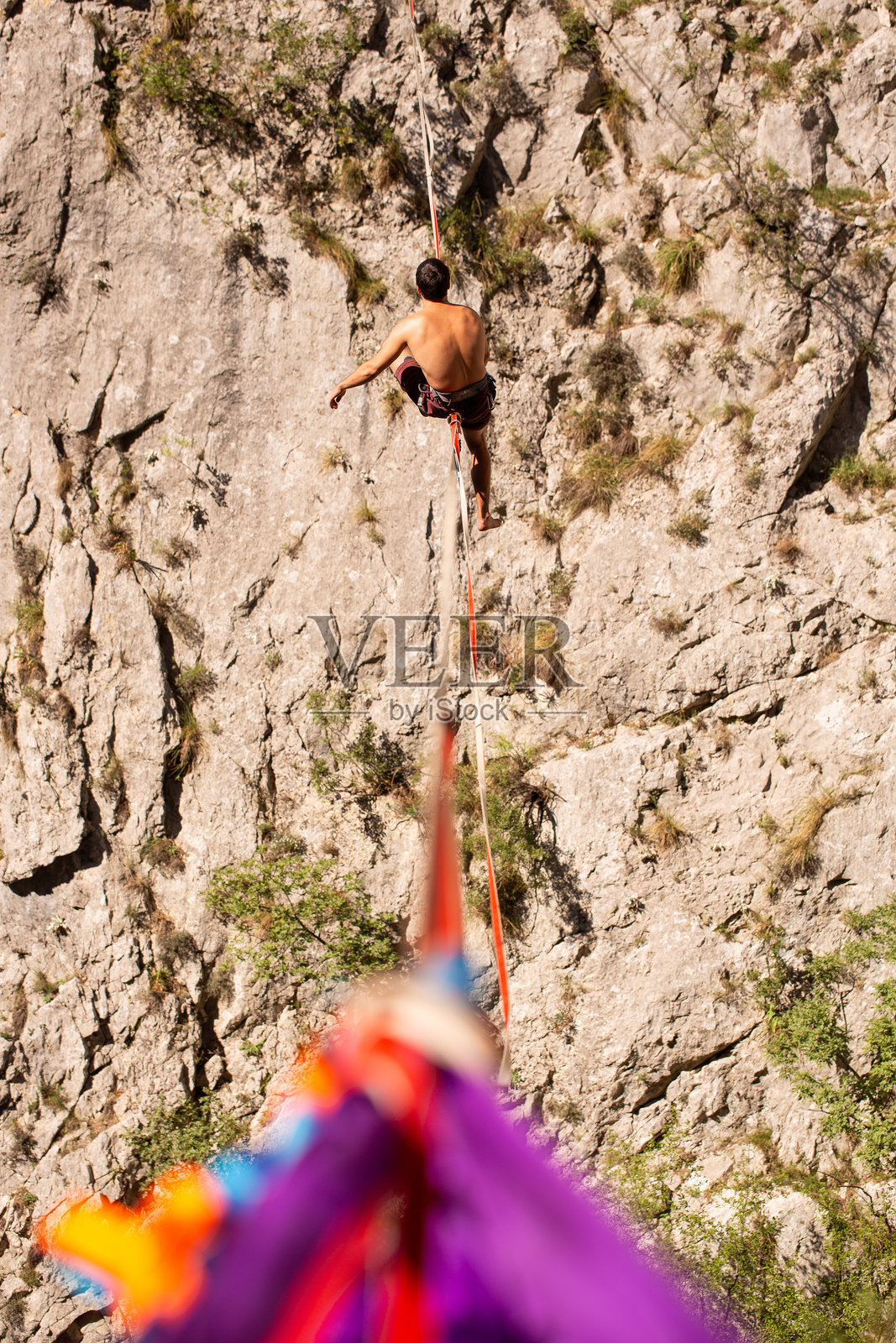 晴朗天气下,一个人在高耸的岩石悬崖上的钢丝上行走,户外自然风光照片摄影图片