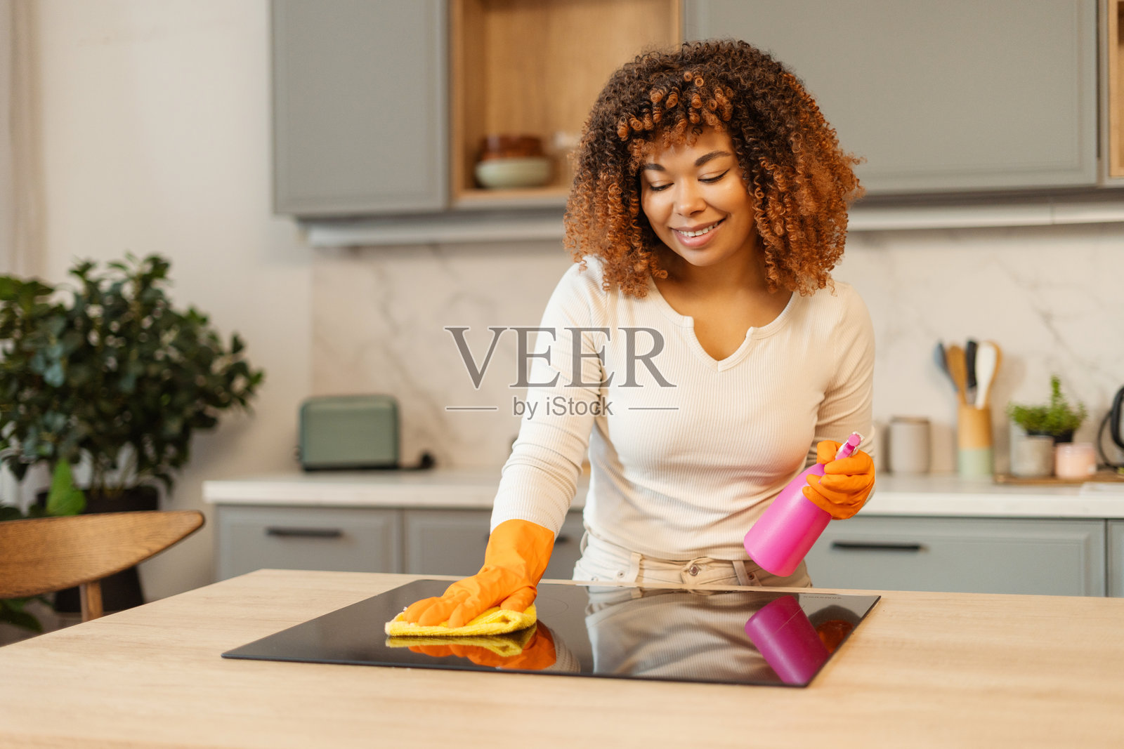 年轻女子在现代厨房里戴着橙色手套清洁电磁炉照片摄影图片