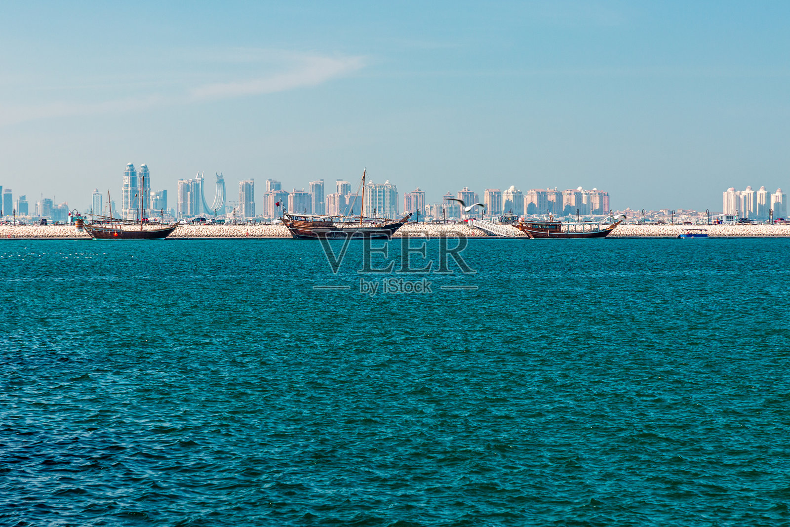 卡塔尔多哈海港的船只,背景是城市天际线,平静的蓝色大海在晴朗的天空下照片摄影图片