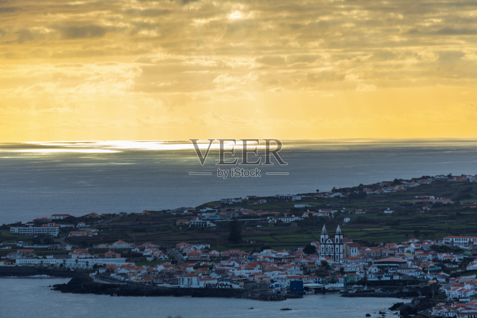 葡萄牙亚速尔群岛特塞拉岛昂格拉杜英雄市的日落航拍景象,温暖的金光照亮了城镇、海岸线和连绵起伏的绿色山丘。照片摄影图片