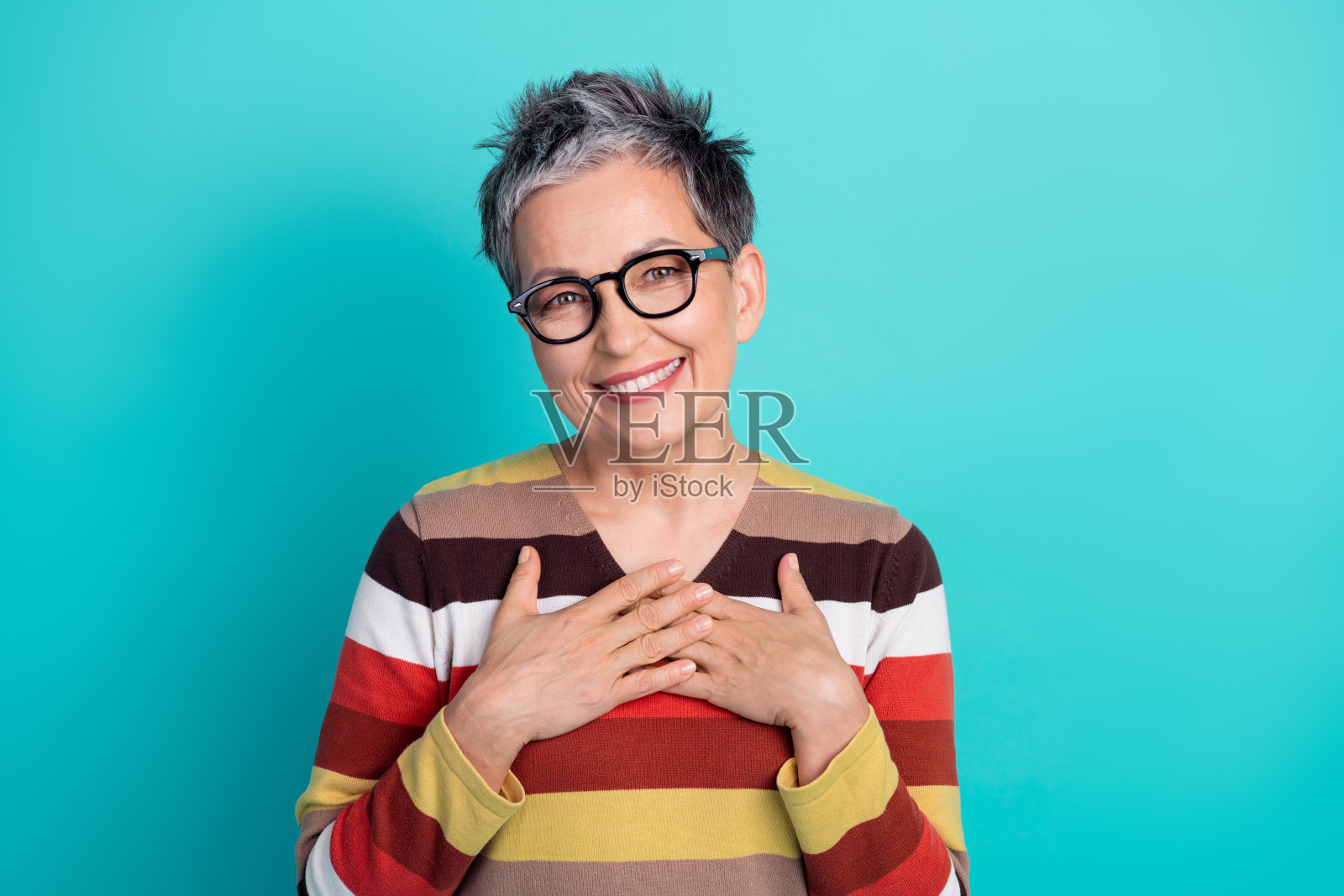 一位留着短灰发、戴着眼镜、穿着彩色条纹毛衣的成熟的女性,在蓝色背景前,面带微笑,展现出快乐、温暖和自信。照片摄影图片