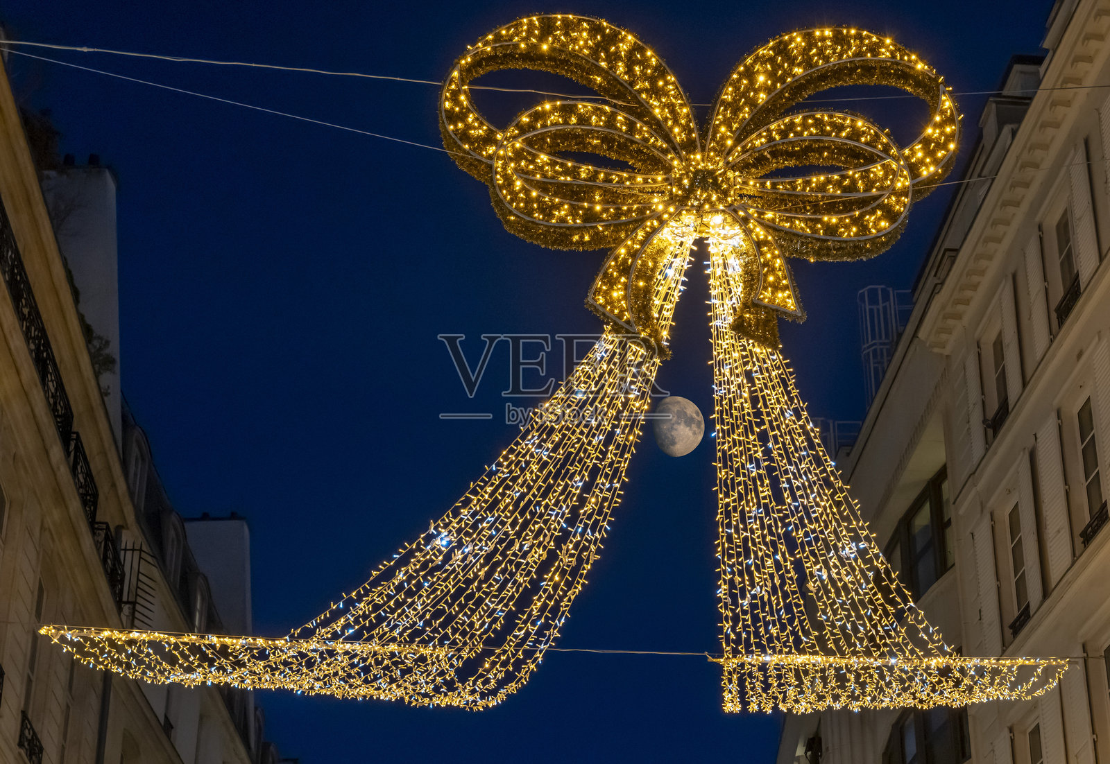 法国巴黎 - 2025年11月30日:挂在街道上方的金色装饰圣诞花环的细节,背景中还有月亮。照片摄影图片