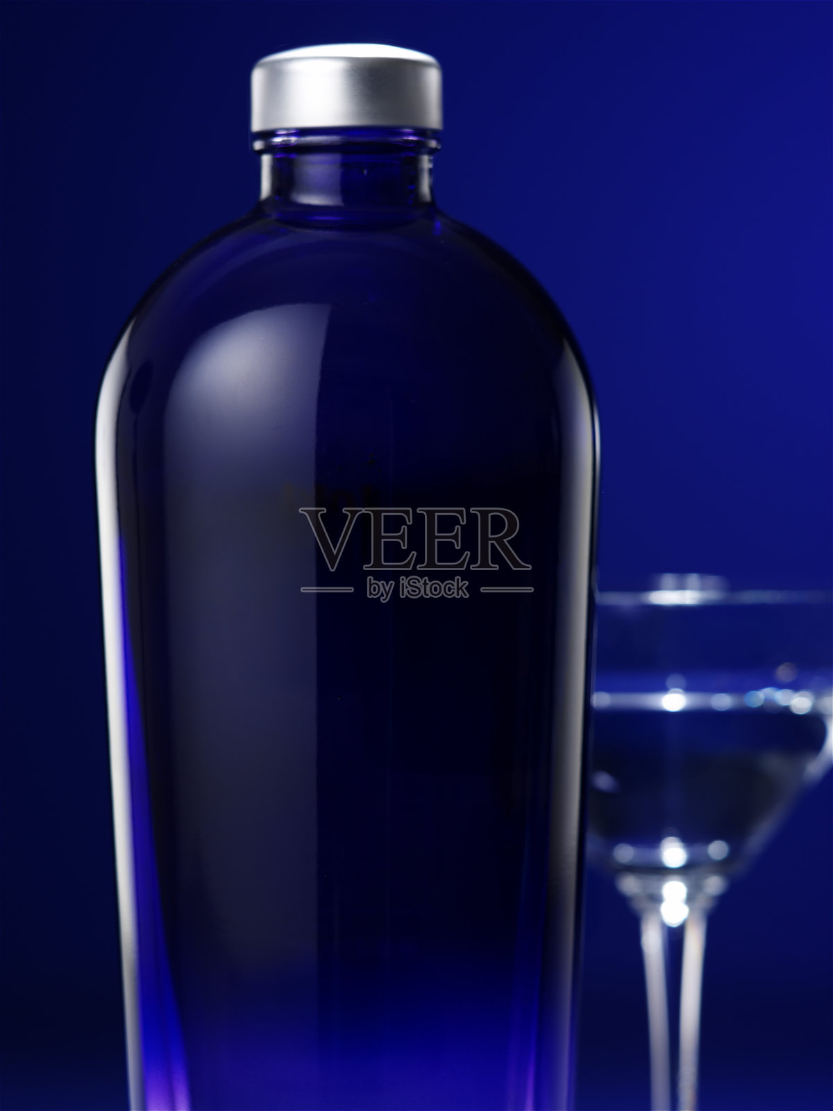 深邃蓝色酒瓶与鸡尾酒杯,置于富有戏剧性的彩色背景上照片摄影图片