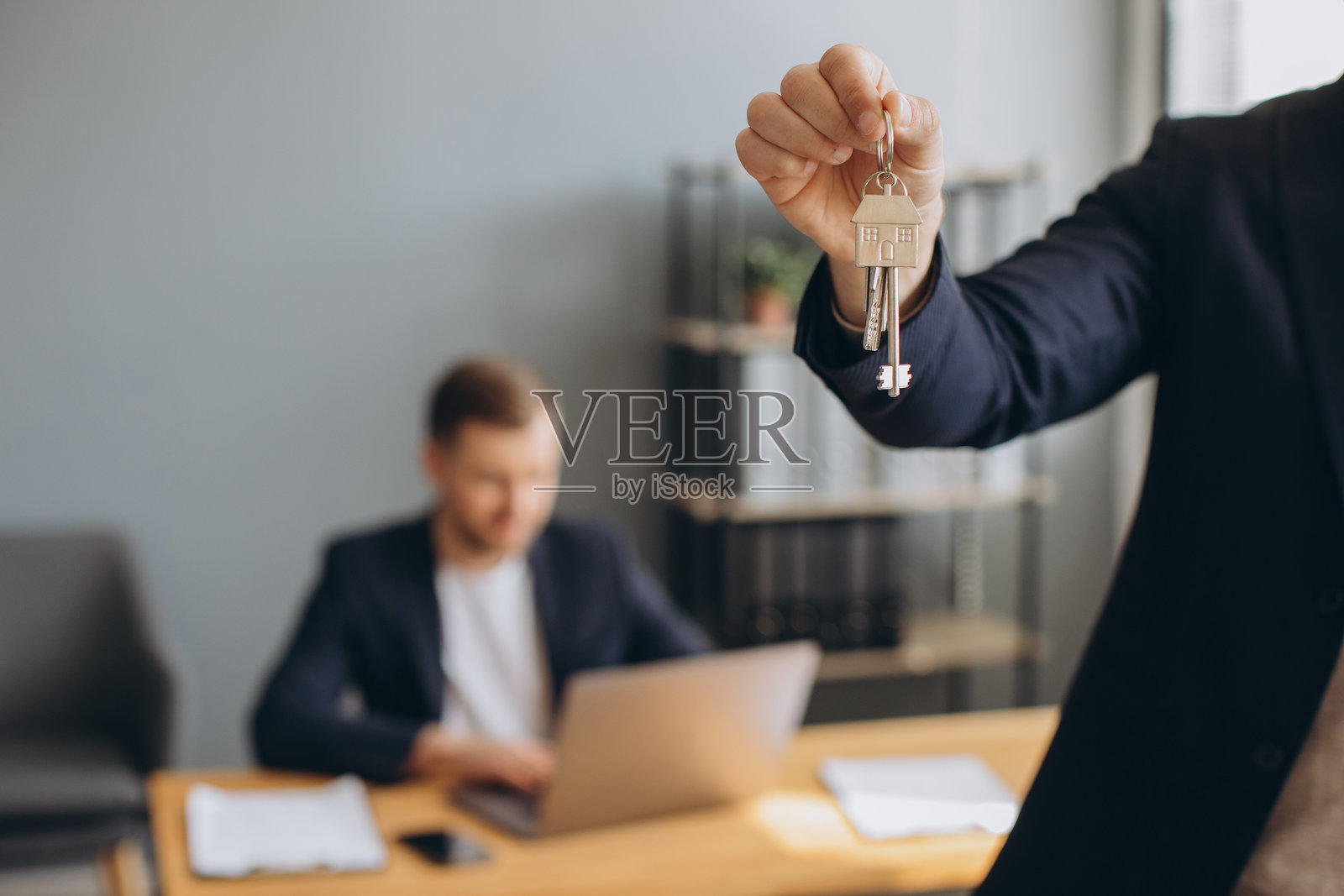 男房产经纪人拿着带房屋挂饰的钥匙,象征着成功的购房交易和新房主的入住照片摄影图片