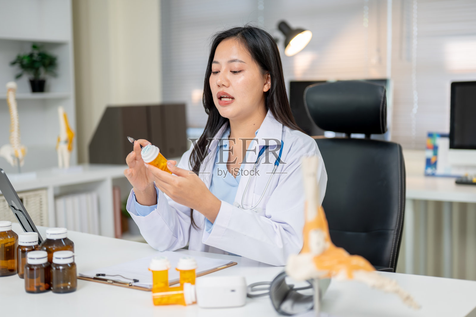 年轻的亚洲女医生在诊断室的工作桌旁查看或阅读药瓶标签照片摄影图片