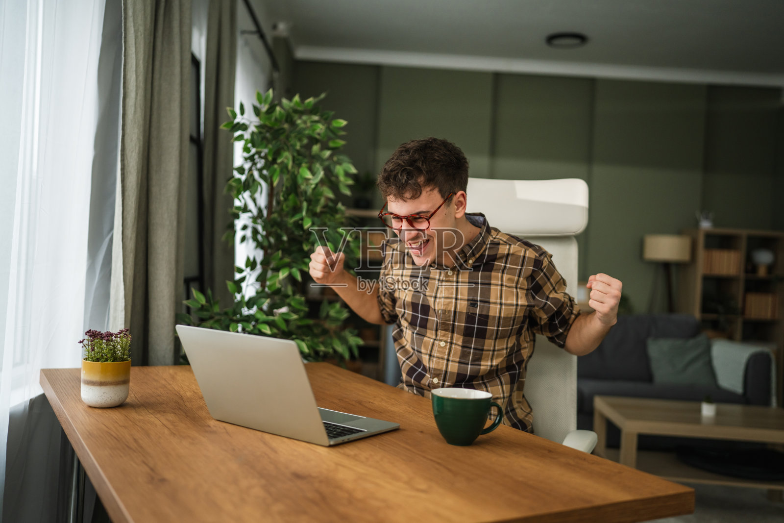 年轻人在家庭办公室的桌子前庆祝在线成功照片摄影图片