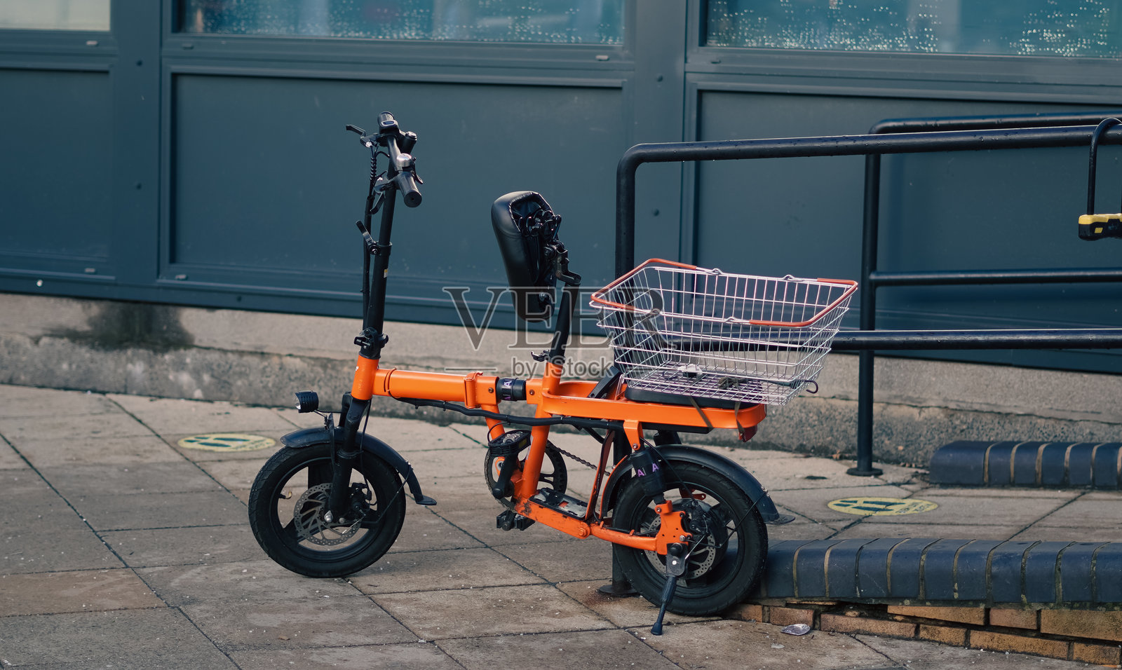 紧凑型橙色电动自行车停在城市人行道上,车篮已装好照片摄影图片