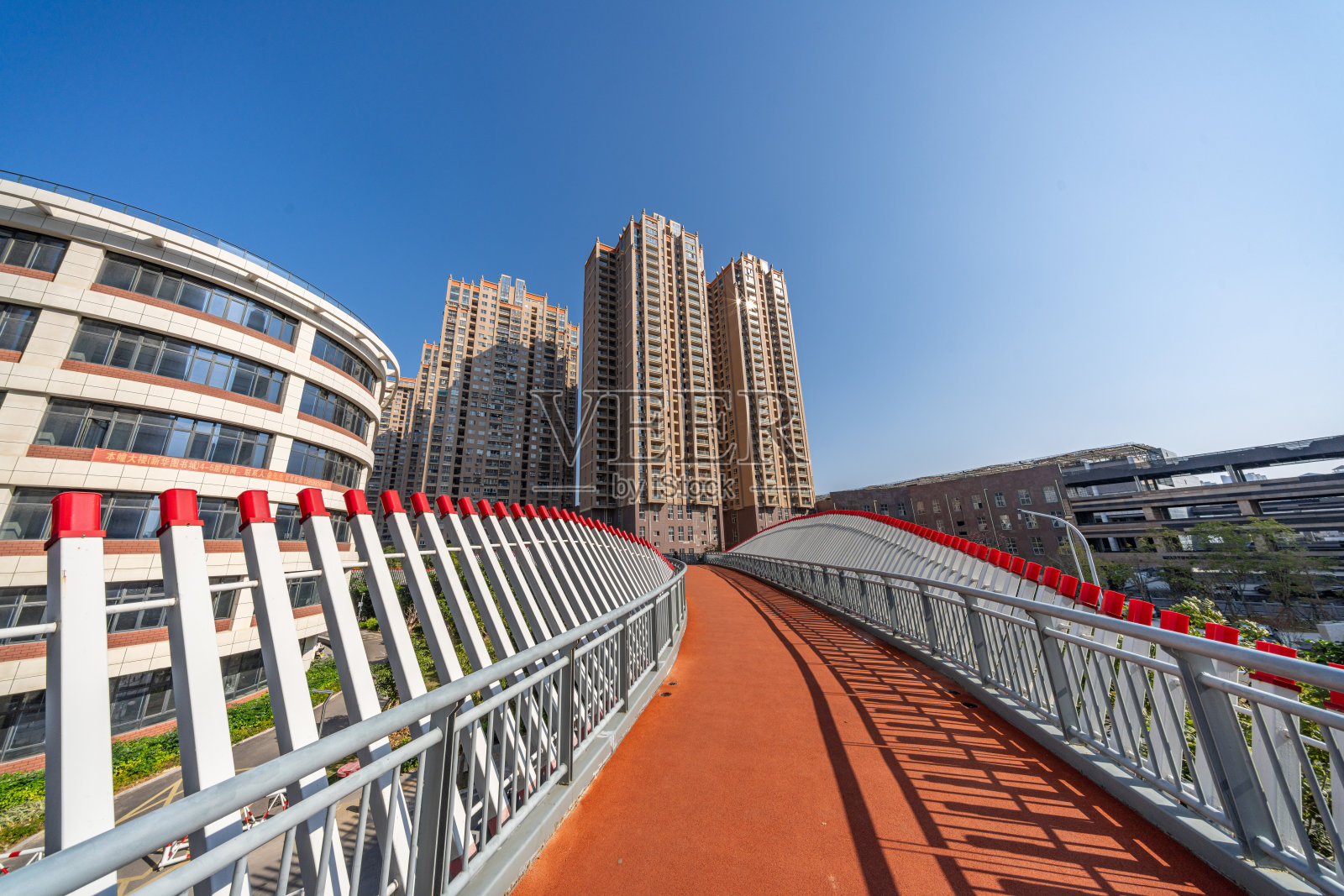 红色沥青路上的行人天桥和周围的城市建筑照片摄影图片