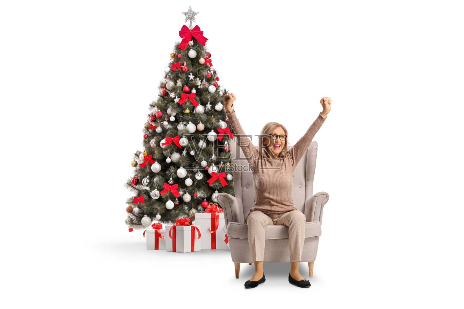 一位中年女性兴奋地坐在圣诞树旁的扶手椅上照片摄影图片