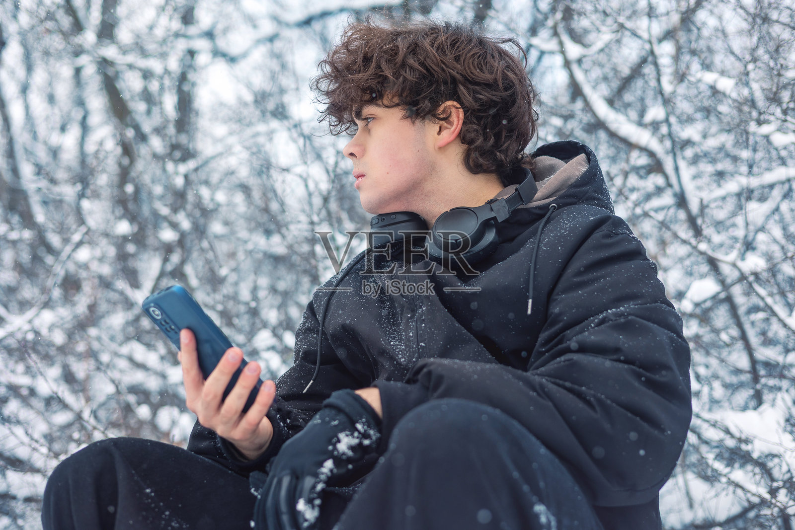 雪地冬林里使用智能手机的青少年男孩,Z世代数字生活方式,移动技术和社交媒体照片摄影图片