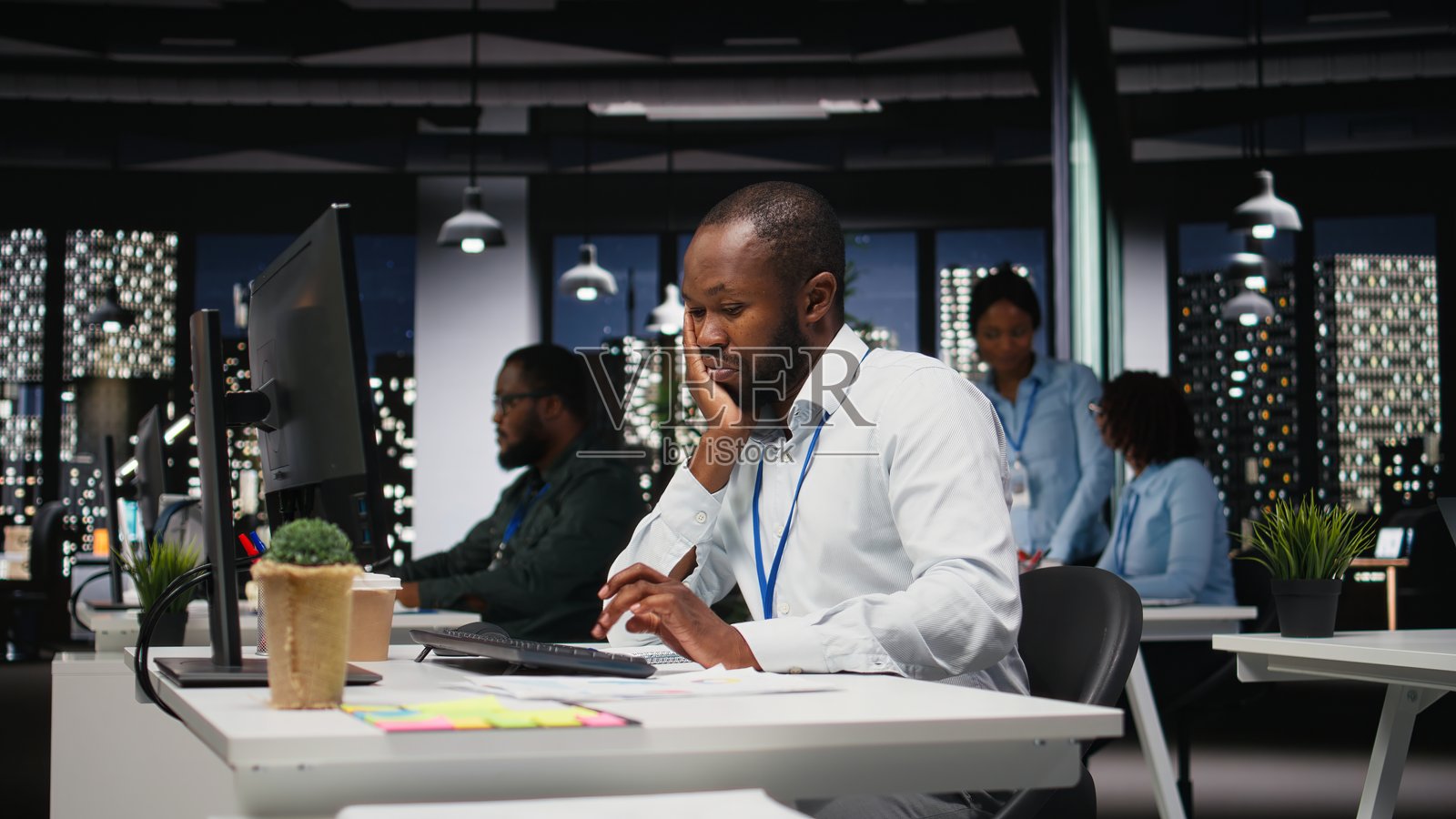 一位非裔美国雇员在昏暗的办公室里疲惫地工作照片摄影图片