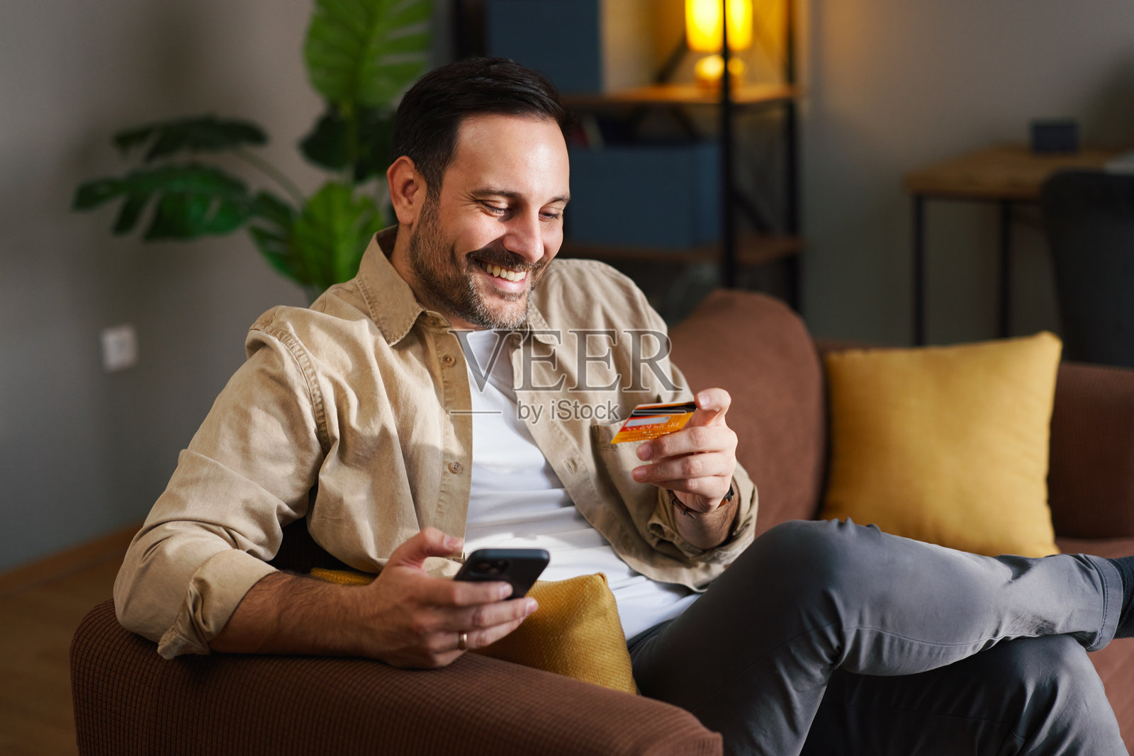男人放松地坐在沙发上,用智能手机和信用卡进行在线支付照片摄影图片