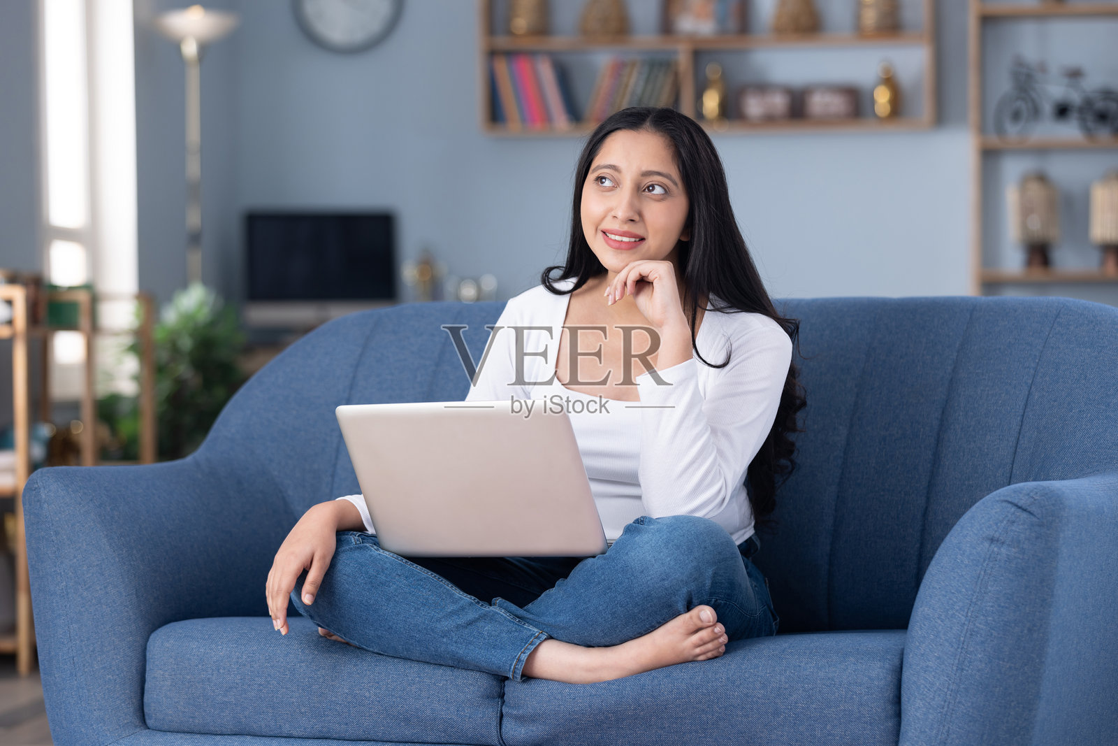 照片:身穿现代服装的漂亮年轻女孩在家中坐在沙发上使用笔记本电脑照片摄影图片