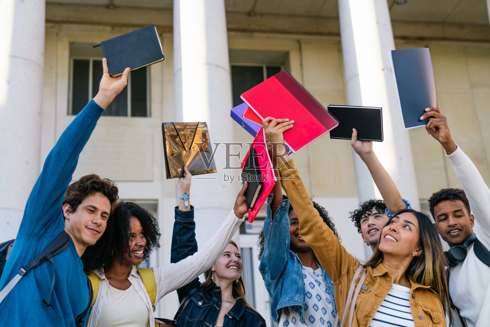 一群来自不同背景的学生在户外举起笔记本,欢庆成功。照片摄影图片
