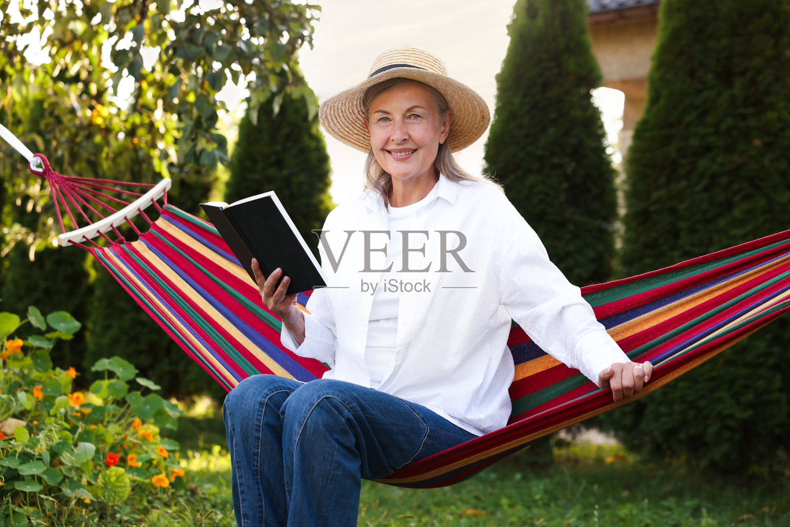 戴草帽的年长女性在户外吊床上阅读照片摄影图片
