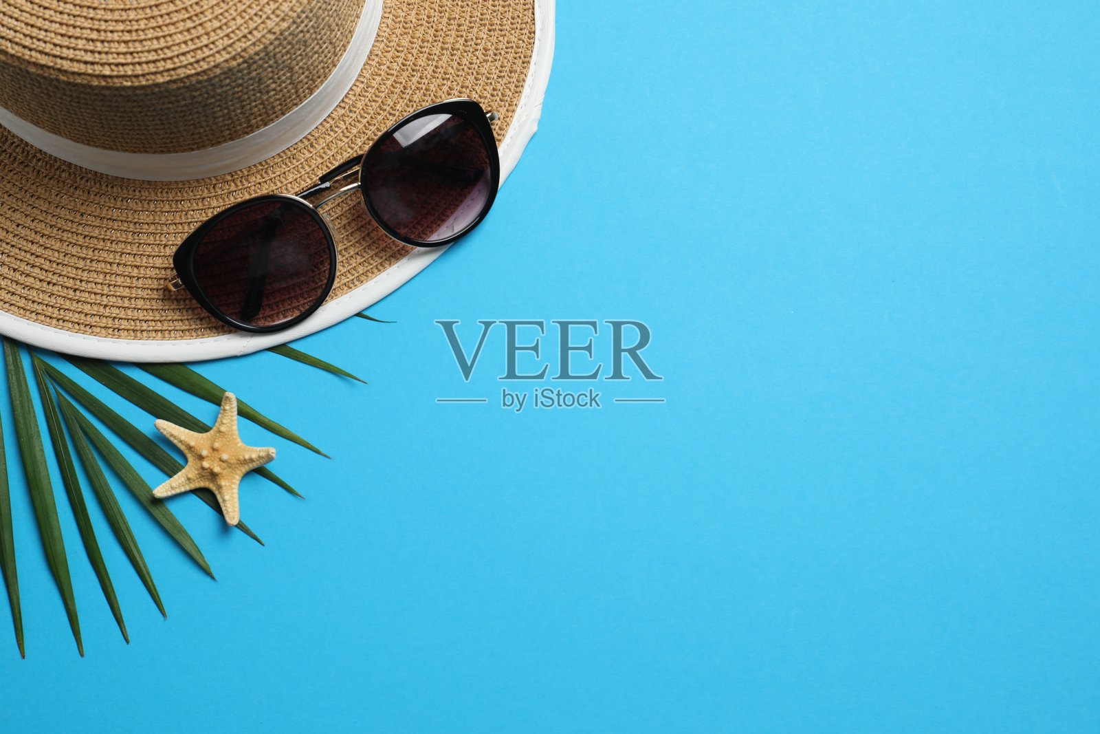蓝色背景下的草帽、太阳镜和棕榈叶平面图。度假概念,俯视图照片摄影图片