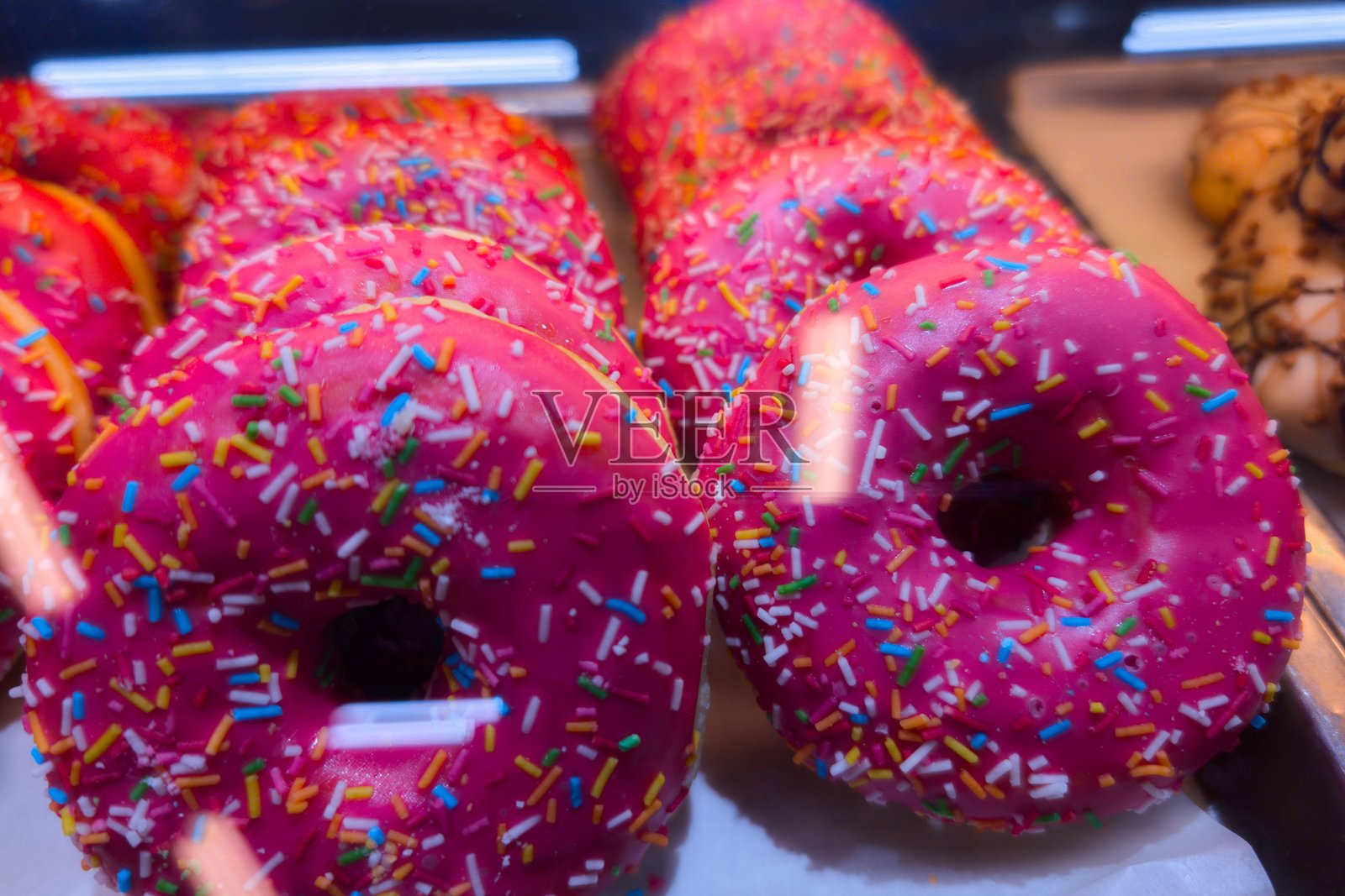 一家烘焙店的玻璃柜中展示着色彩缤纷的带糖珠的粉色甜甜圈照片摄影图片