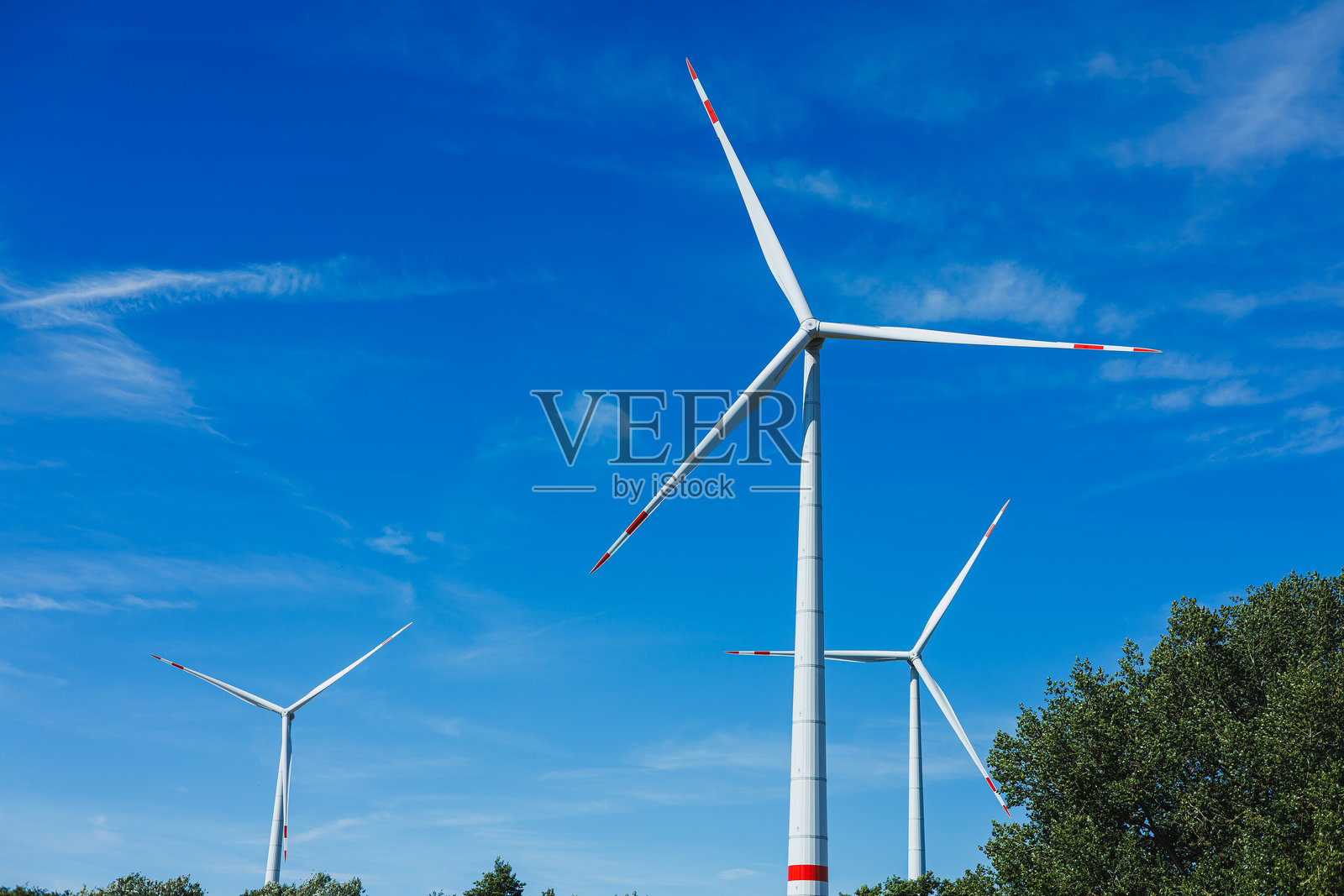 白天,在乡村景观中,三座大型风力涡轮机在明亮的蓝天下矗立。照片摄影图片