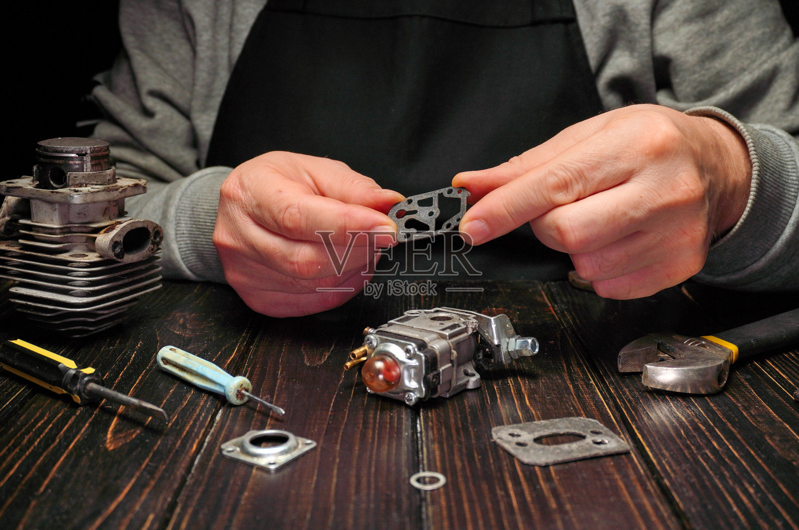 一个人坐在木桌旁,专注于修理发动机零件。周围摆放着工具和各种组件,展示了维护的过程。照片摄影图片