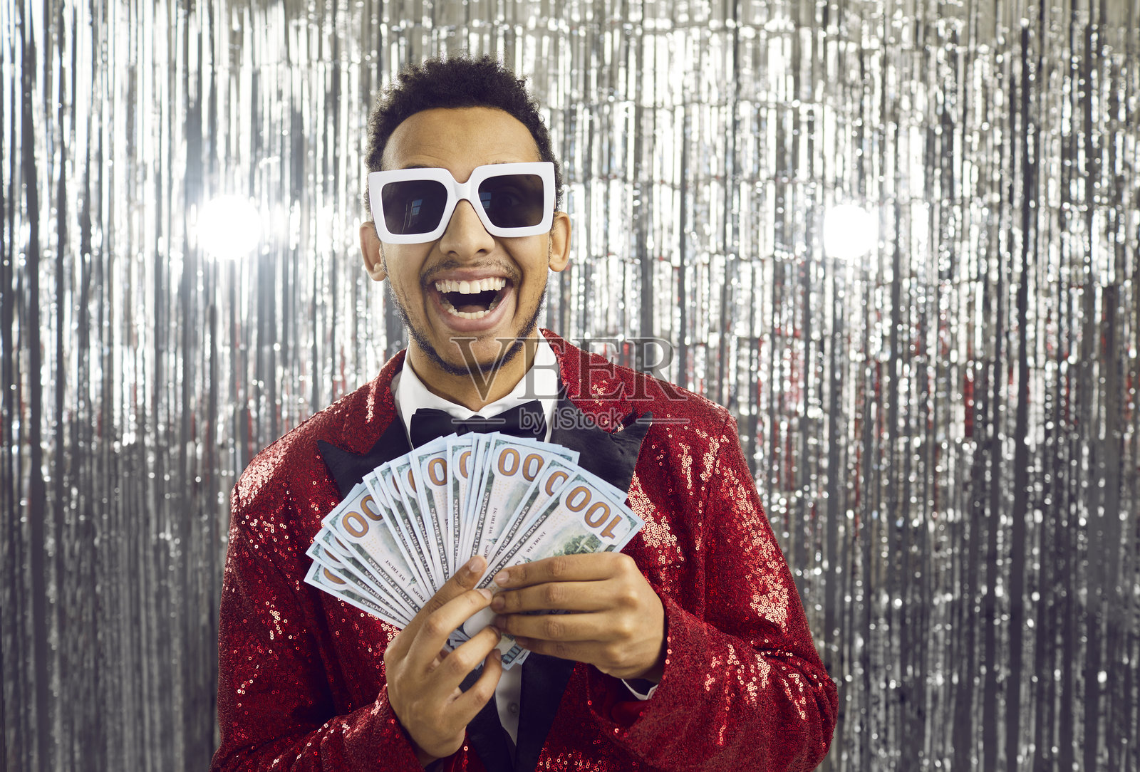 兴奋快乐的年轻非裔美国人表演者,手中拿着美元钞票,背景为闪亮的银色。照片摄影图片