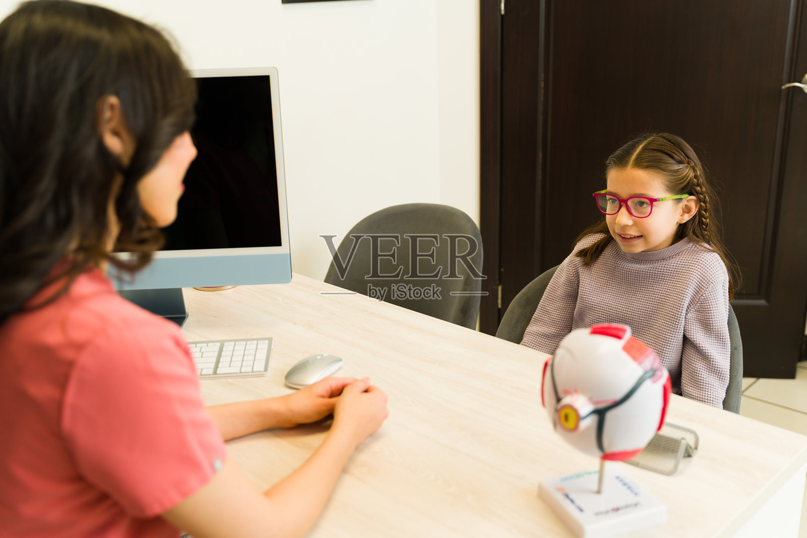 眼科医生在医疗咨询中与一个小女孩谈论眼部护理、视力健康和眼镜照片摄影图片