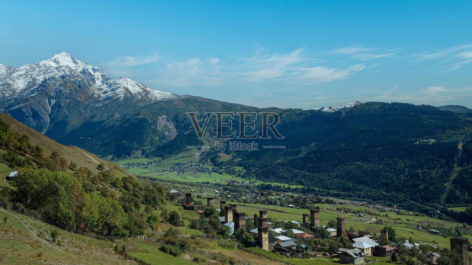 雪山之巅下,一座古老的山村,拥有中世纪风格的塔楼,天空湛蓝。照片摄影图片