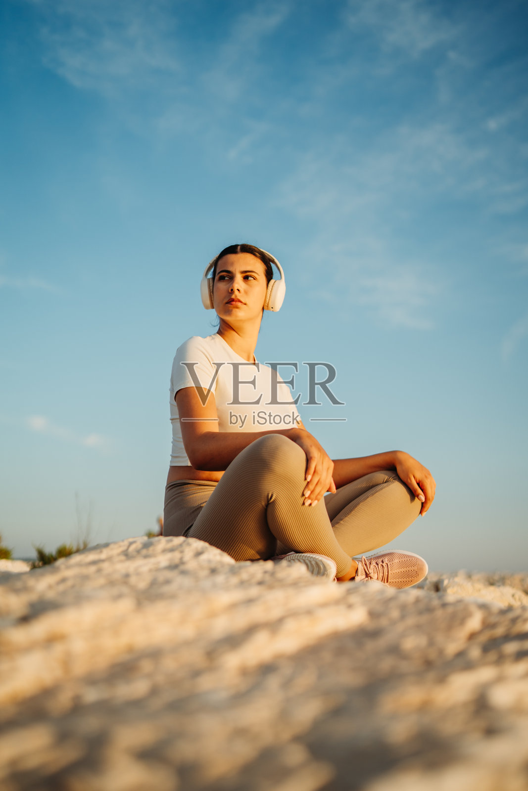 女子戴着耳机在日落时分岩石上冥想照片摄影图片