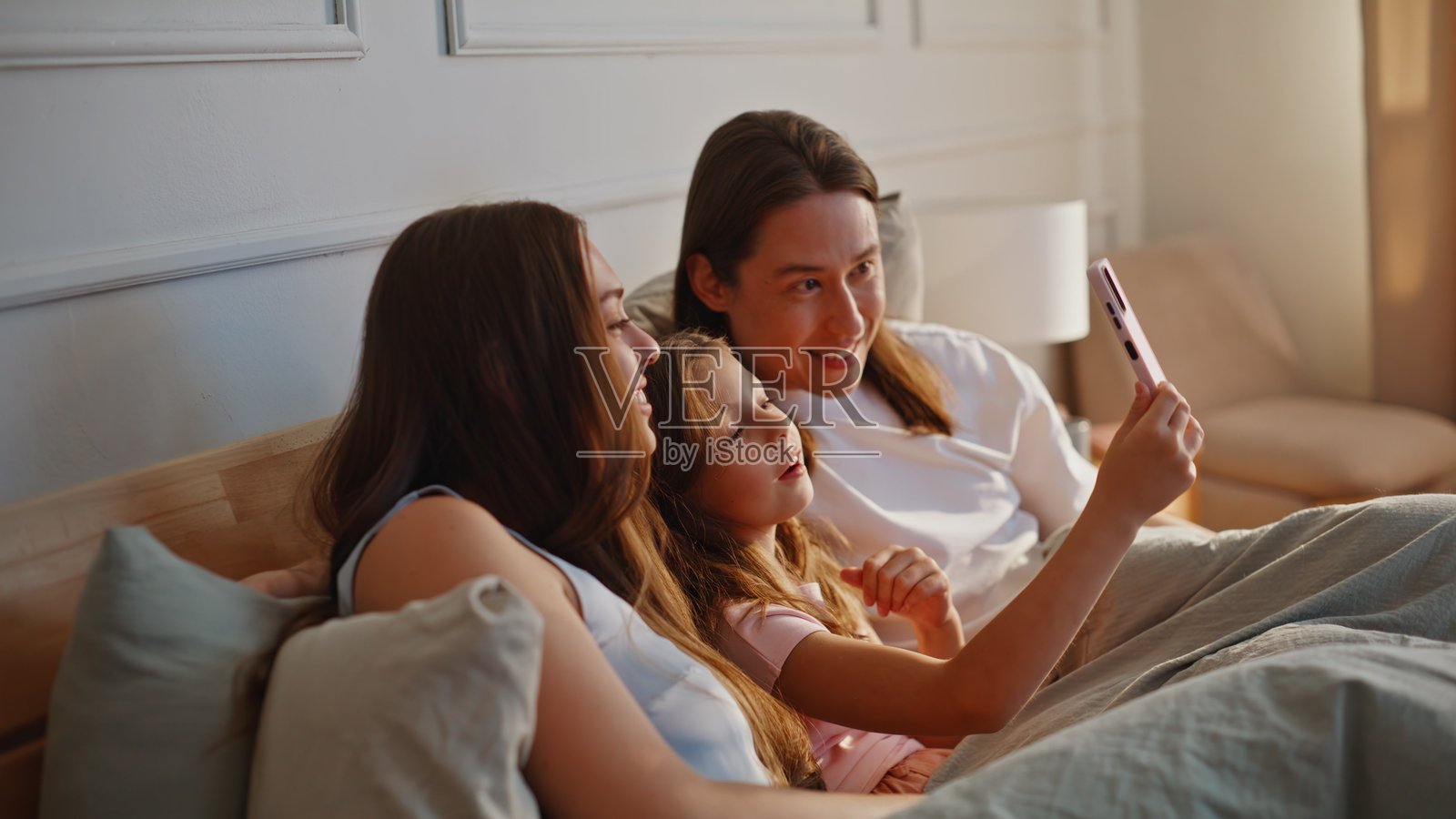 阳光明媚的卧室里,一家人快乐地使用智能手机拍照,特写镜头照片摄影图片