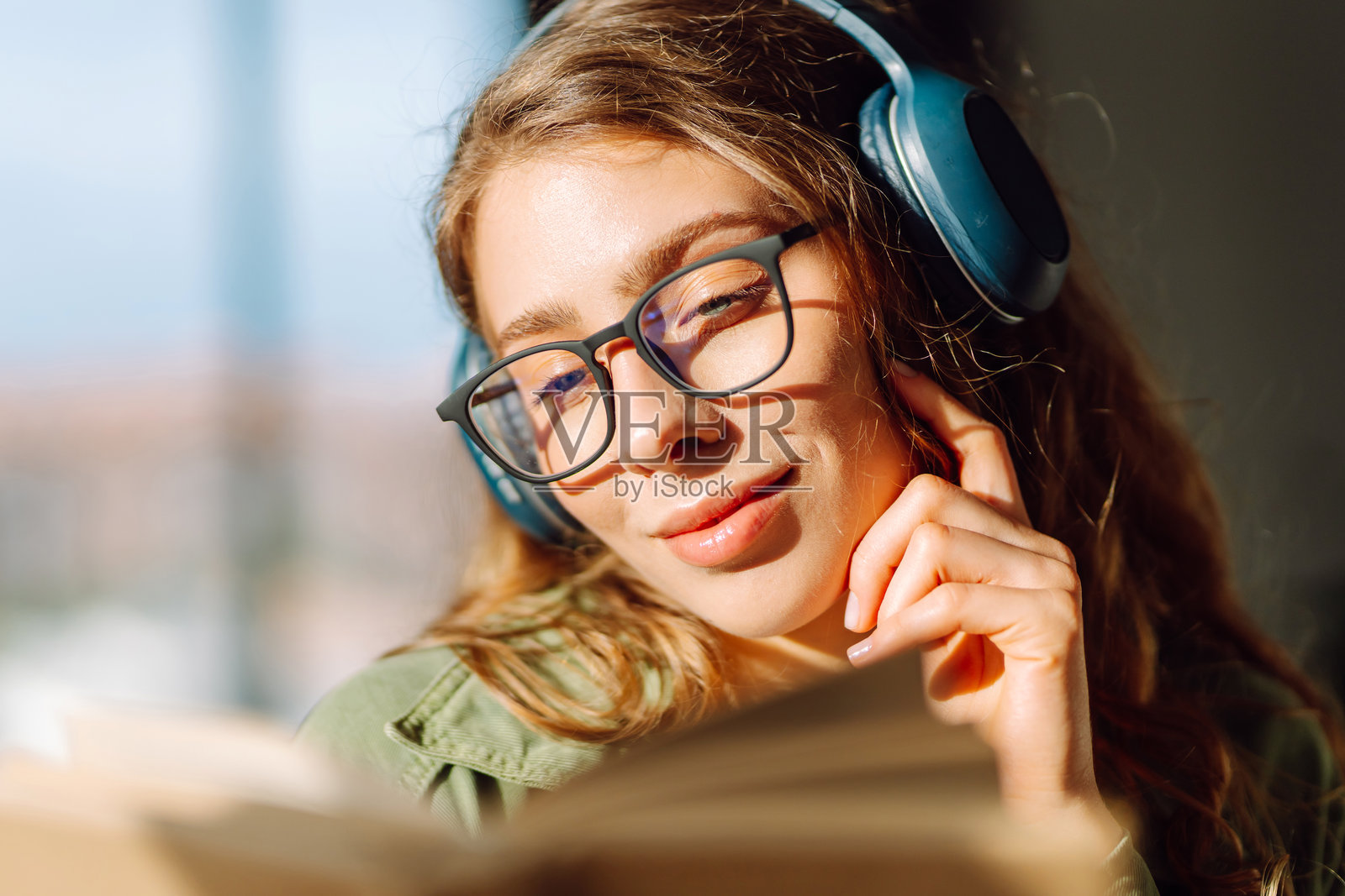 舒适房间里,一位戴着无线耳机看书的女性的特写。照片摄影图片