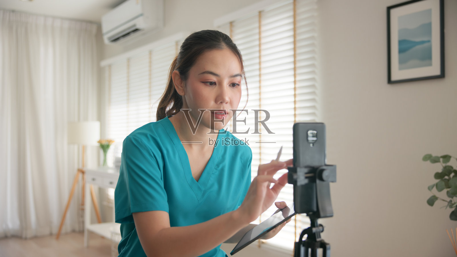 年轻的亚洲Z世代女性,抗衰老专家,现代护士,正在通过手机APP为直播或自拍视频做准备,进行在线副业,数字虚拟亚洲Vlogger拍摄。照片摄影图片