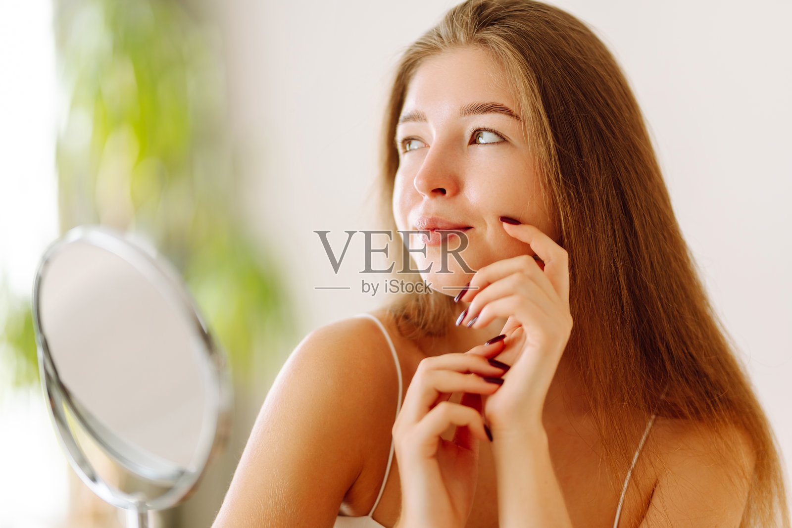 一位甜美的女士坐在小镜子前,在阳光下用手指触摸脸庞。照片摄影图片