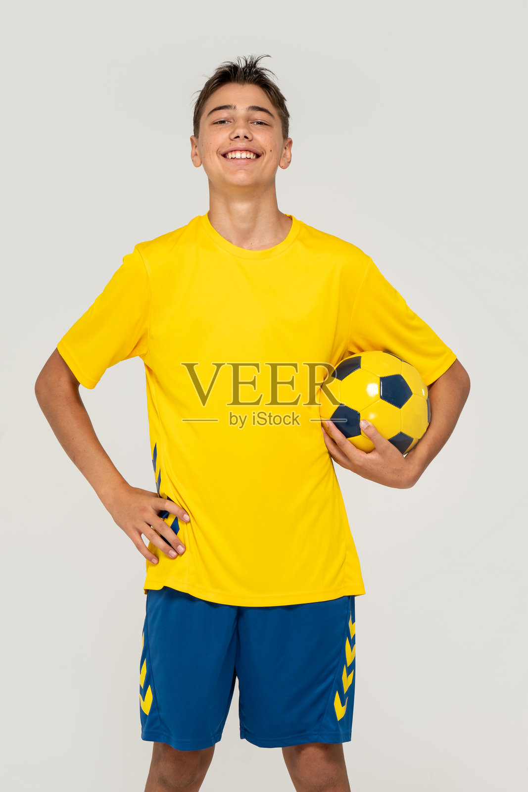 穿着运动服、面带笑容的快乐少年抱着足球看向镜头照片摄影图片