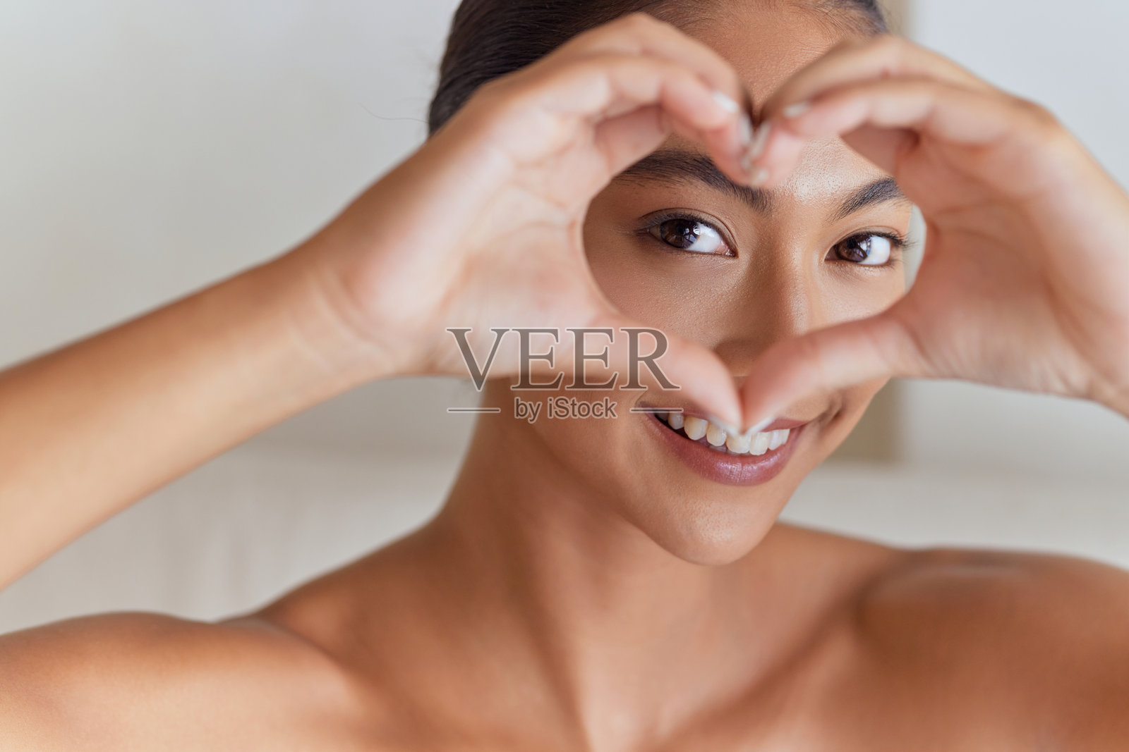 微笑的女人用手比心形,围绕着眼睛照片摄影图片