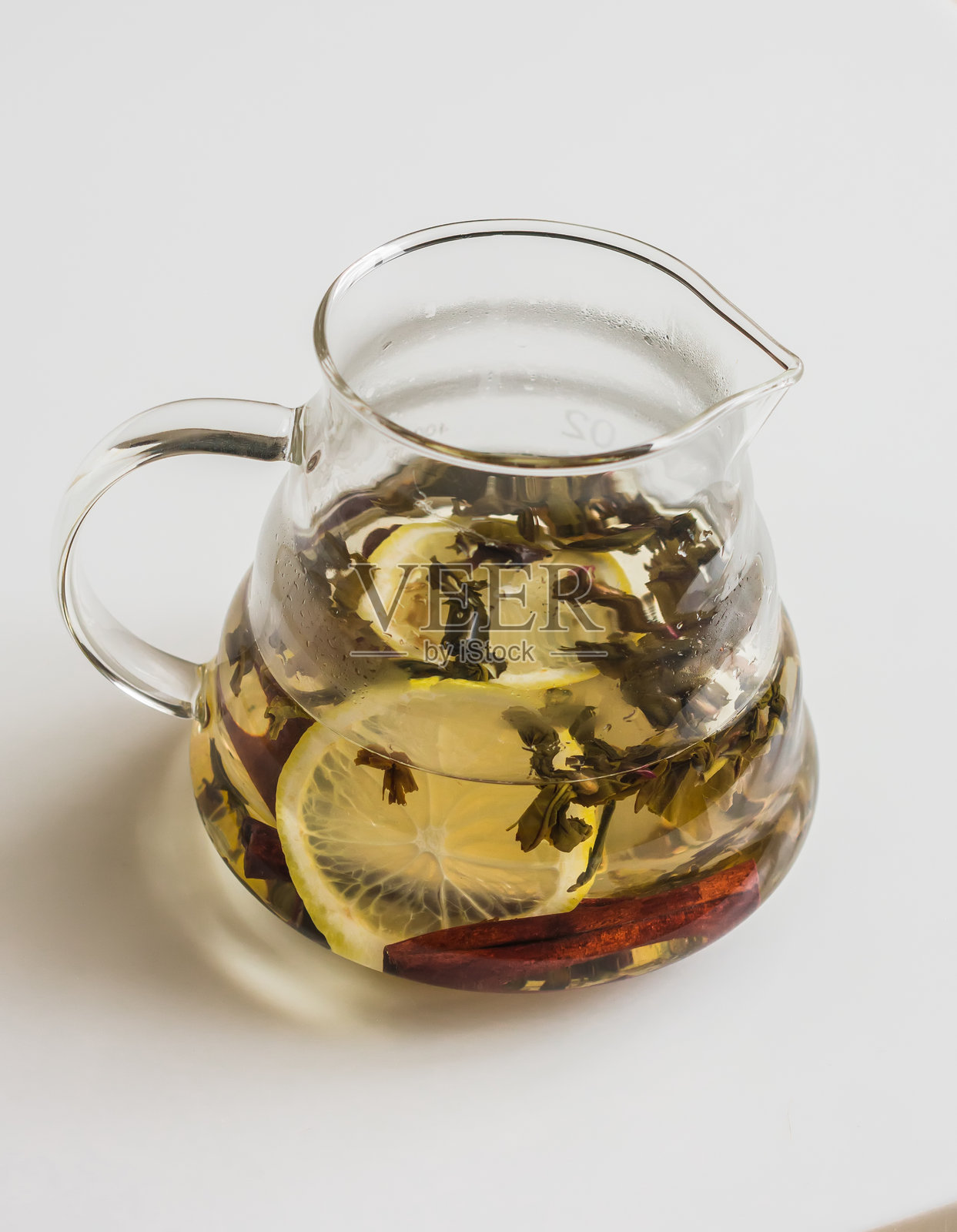 玻璃茶壶中盛有香气浓郁的暖身绿茶,搭配肉桂棒和柠檬,背景浅色,俯视角度照片摄影图片