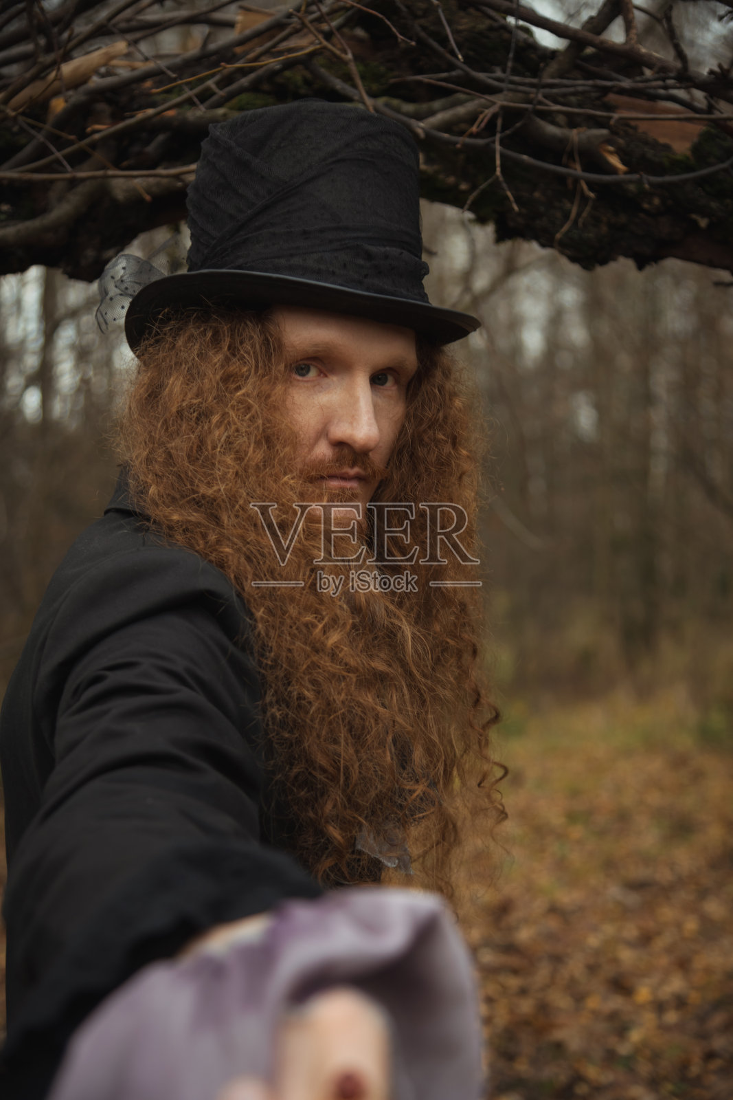 身着礼帽的神秘男子伸出手,置身于诡异的森林之中照片摄影图片