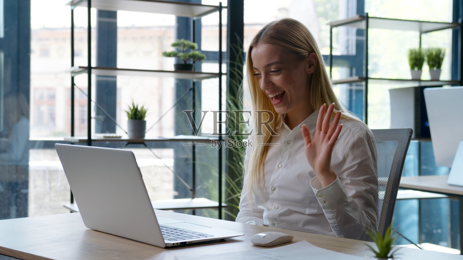一位白种女性兴奋地对着电脑视频通话,面带微笑,享受着在线会议,她在办公室工作、咨询、聊天,是一位满意的女商人正在打招呼。照片摄影图片