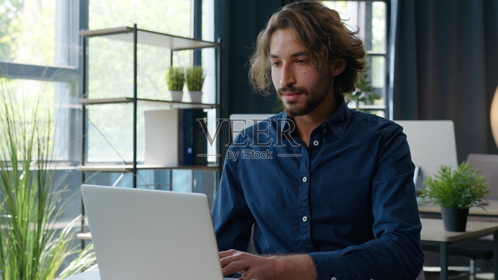 一位西班牙裔男商人在办公室的桌子前工作,他正在打字、看文件、使用电脑分析在线数据,这位经理正在为初创公司开发工作使用在线软件。照片摄影图片