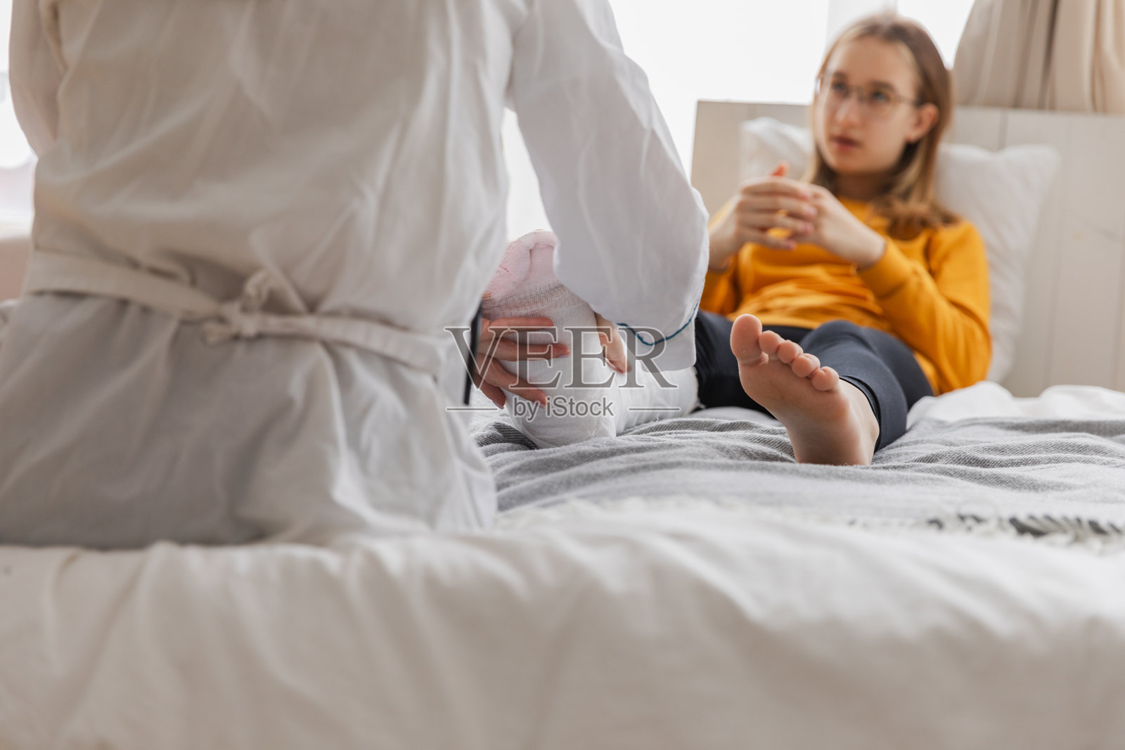 医生的诊所里,一名女孩腿部骨折,创伤科骨科医生正在检查孩子的腿。医生正在为摔断脚踝受伤的女孩进行石膏腿部固定后的检查,进行康复治疗。照片摄影图片