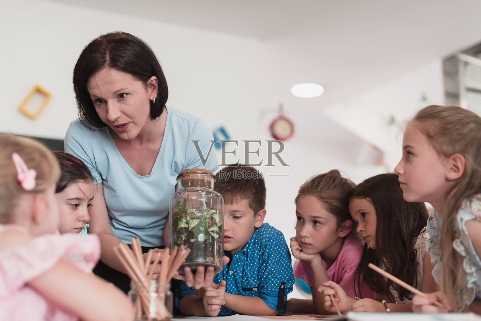 小学女教师在生物课上指导孩子们进行关于可持续植物生长的科学实验,通过玻璃罐学习植物知识。照片摄影图片