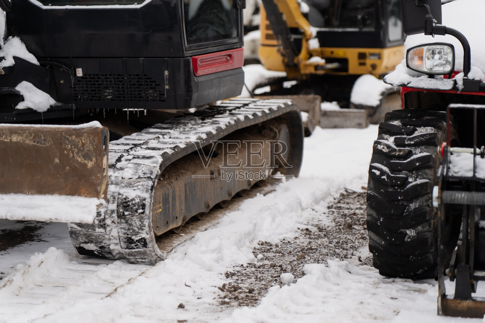 雪地施工现场,挖掘机履带和小型车辆车轮的细节特写,季节为寒冷的冬季照片摄影图片