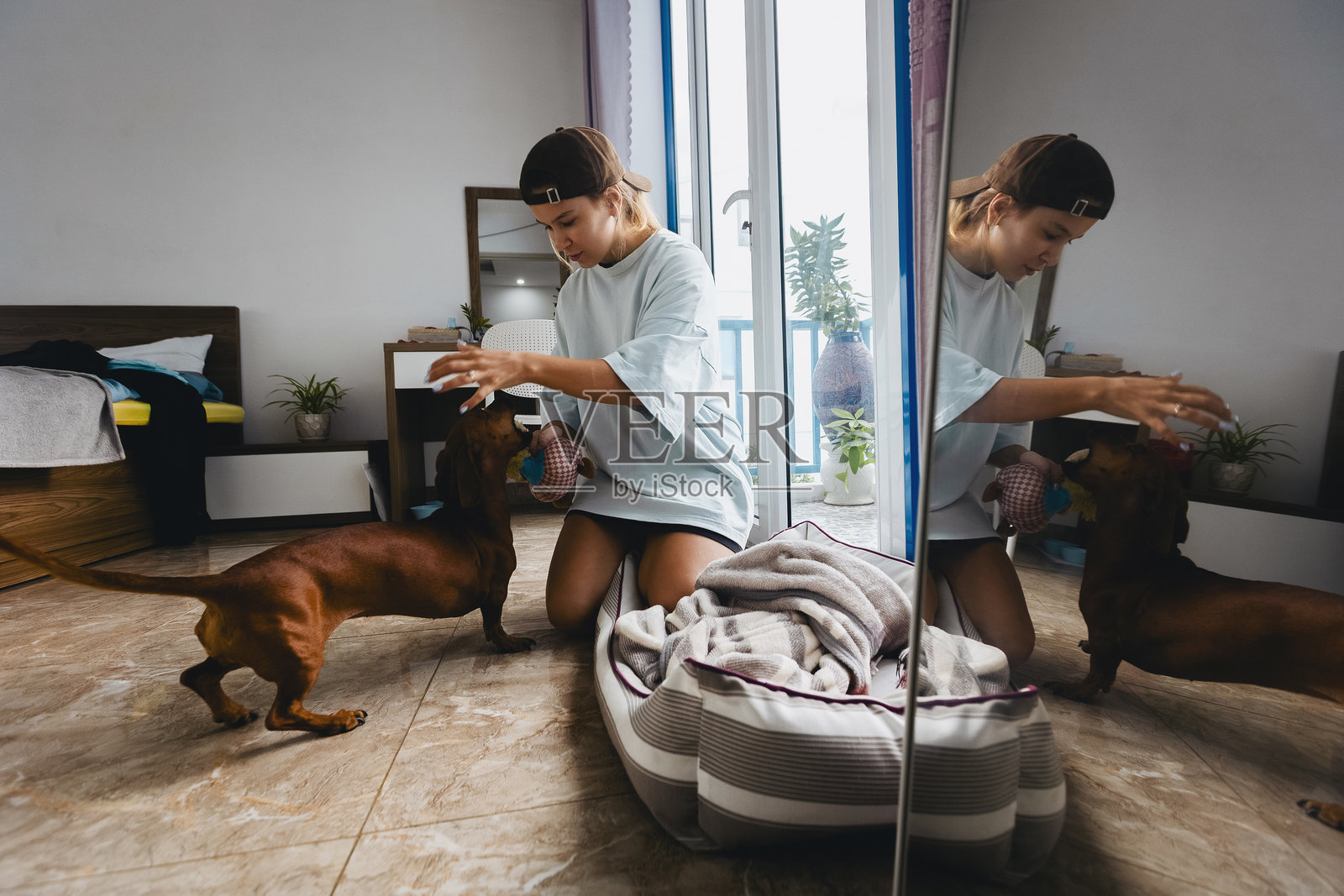 年轻的白人女性在卧室的镜子前与腊肠犬玩耍照片摄影图片