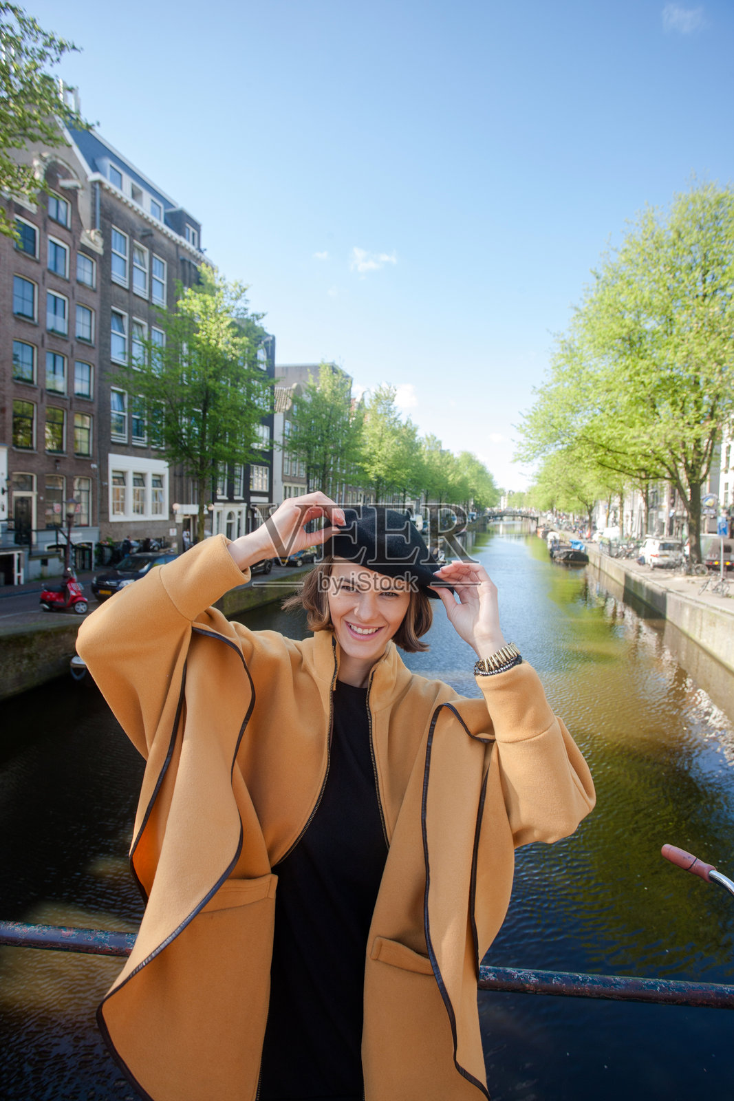 阳光明媚的一天,一位美丽的年轻女子在阿姆斯特丹的运河边摆姿势拍照。照片摄影图片