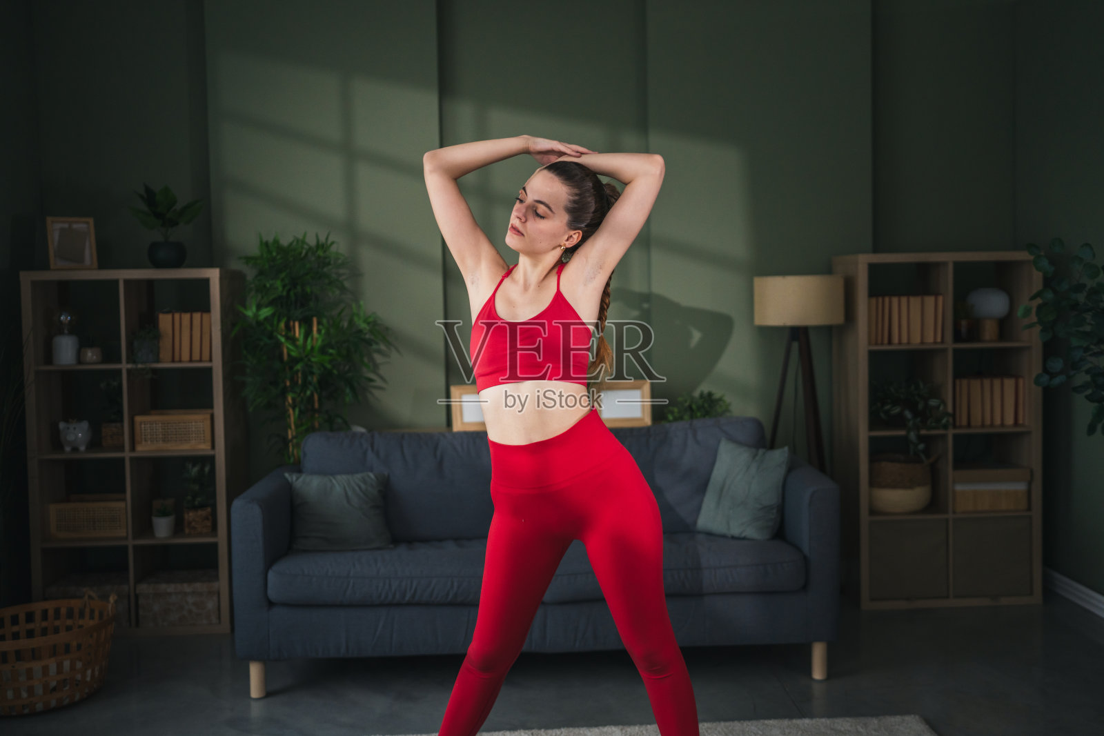身穿红色运动服的年轻女子在家中伸展身体照片摄影图片