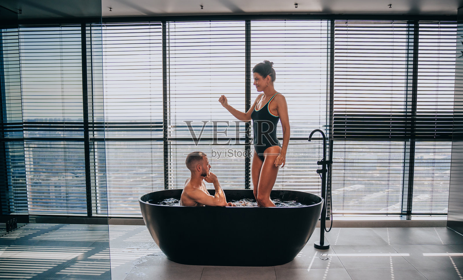 一对情侣正在享受热闹的沐浴时光,充满活力的瞬间,窗外可见繁华的城市景色。照片摄影图片