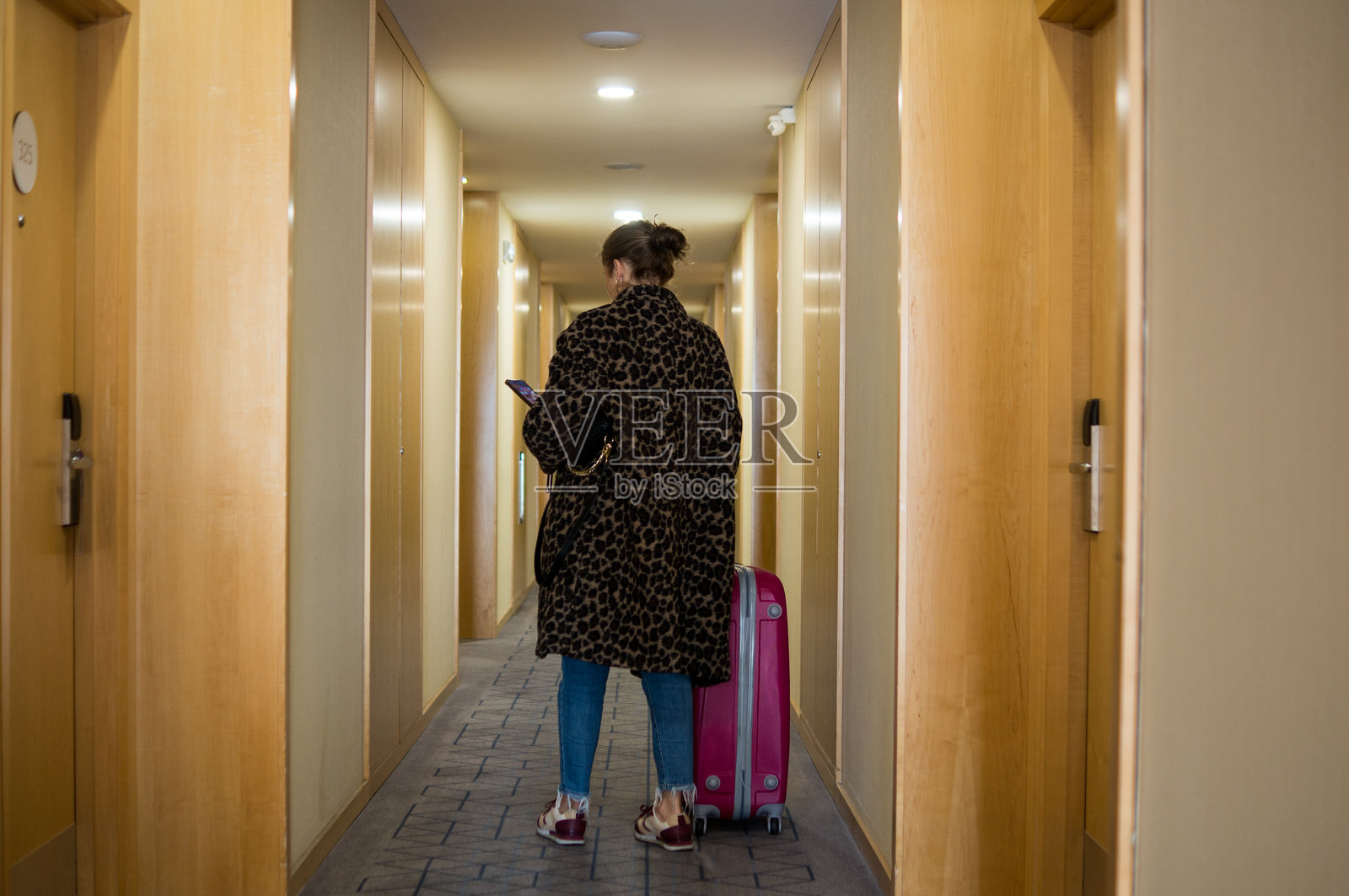 穿着豹纹大衣的单身女游客在酒店走廊查看智能手机照片摄影图片
