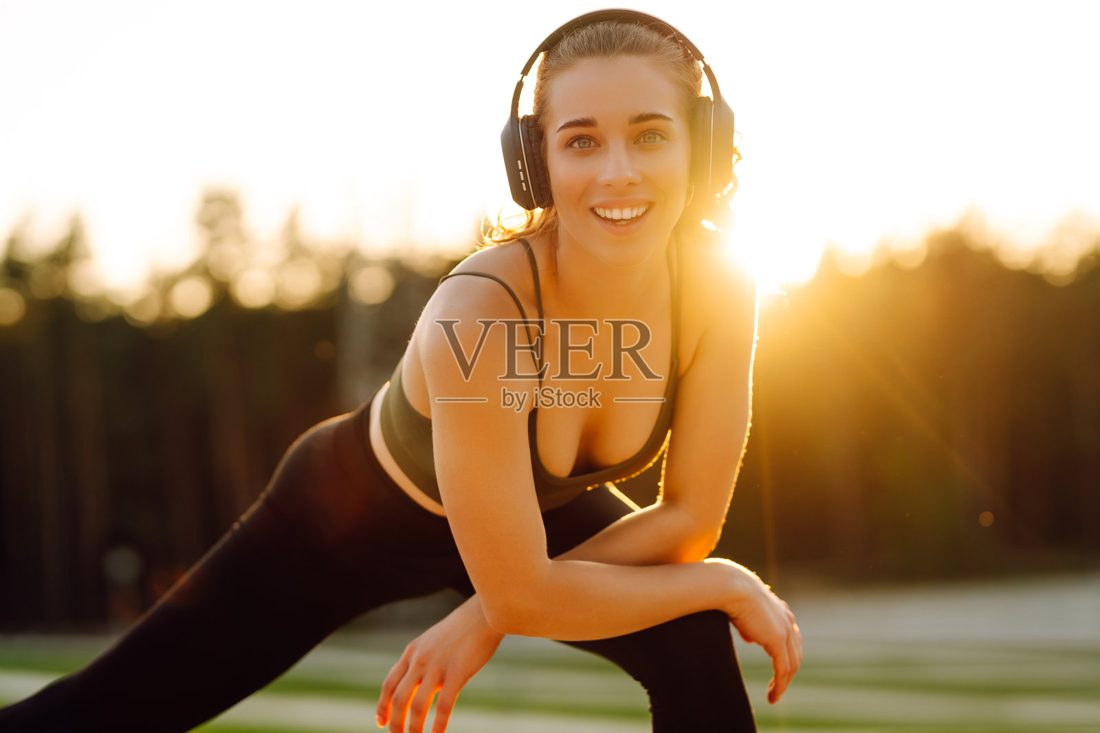 一位运动中的女性戴着无线耳机在阳光下跑步或锻炼前热身。照片摄影图片
