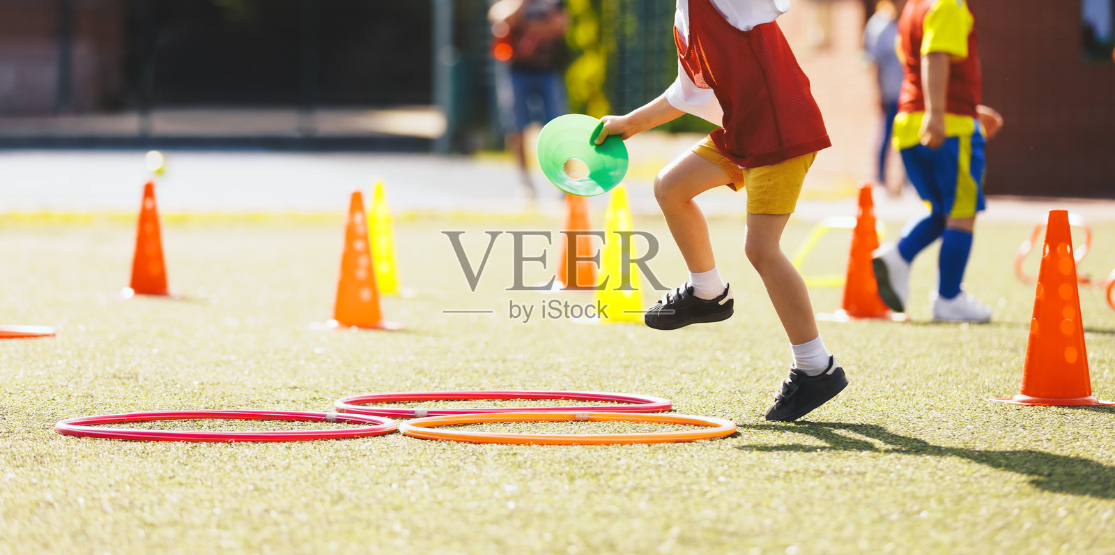 儿童足球装备训练。孩子跳过障碍物。足球速度训练。年轻足球运动员在草地足球场训练课上穿着运动服。照片摄影图片